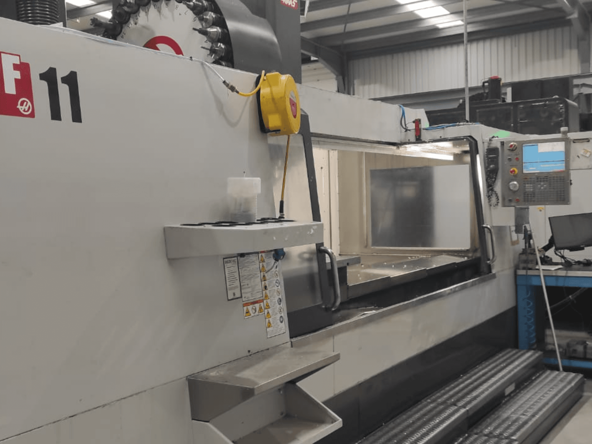 Stroj tvrtke Haas, model VF-11, prikazan s prednje strane s upravljačkom pločom, velikim radnim prostorom i vidljivim sigurnosnim naljepnicama.