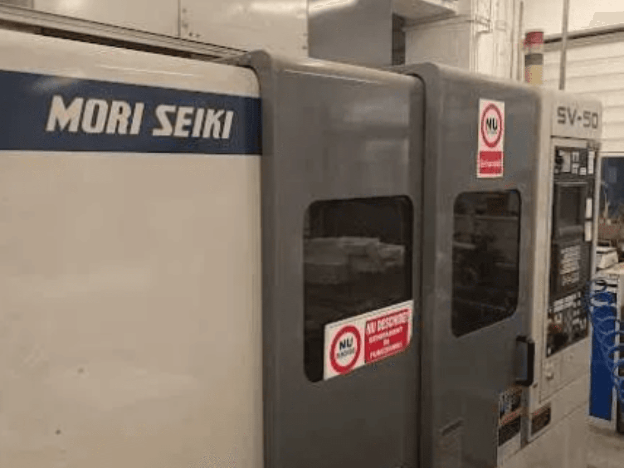 MORI SEIKI SV-50 CNC stroj, bočni pogled; ima upravljačku ploču i naljepnice s sigurnosnim upozorenjima.