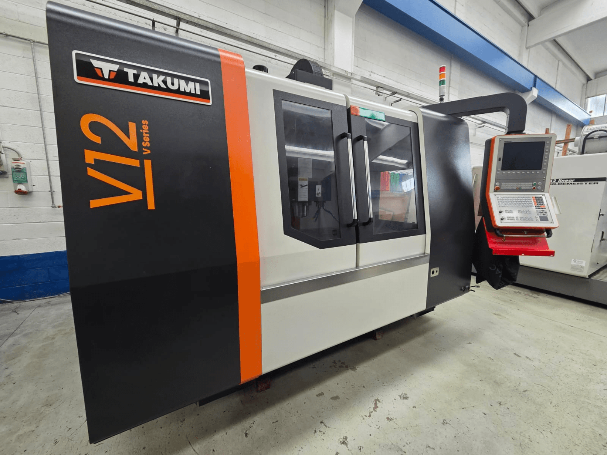 CNC glodalica Takumi V12 serije V, pogled sprijeda, ima upravljačku ploču i velike staklene prozore.