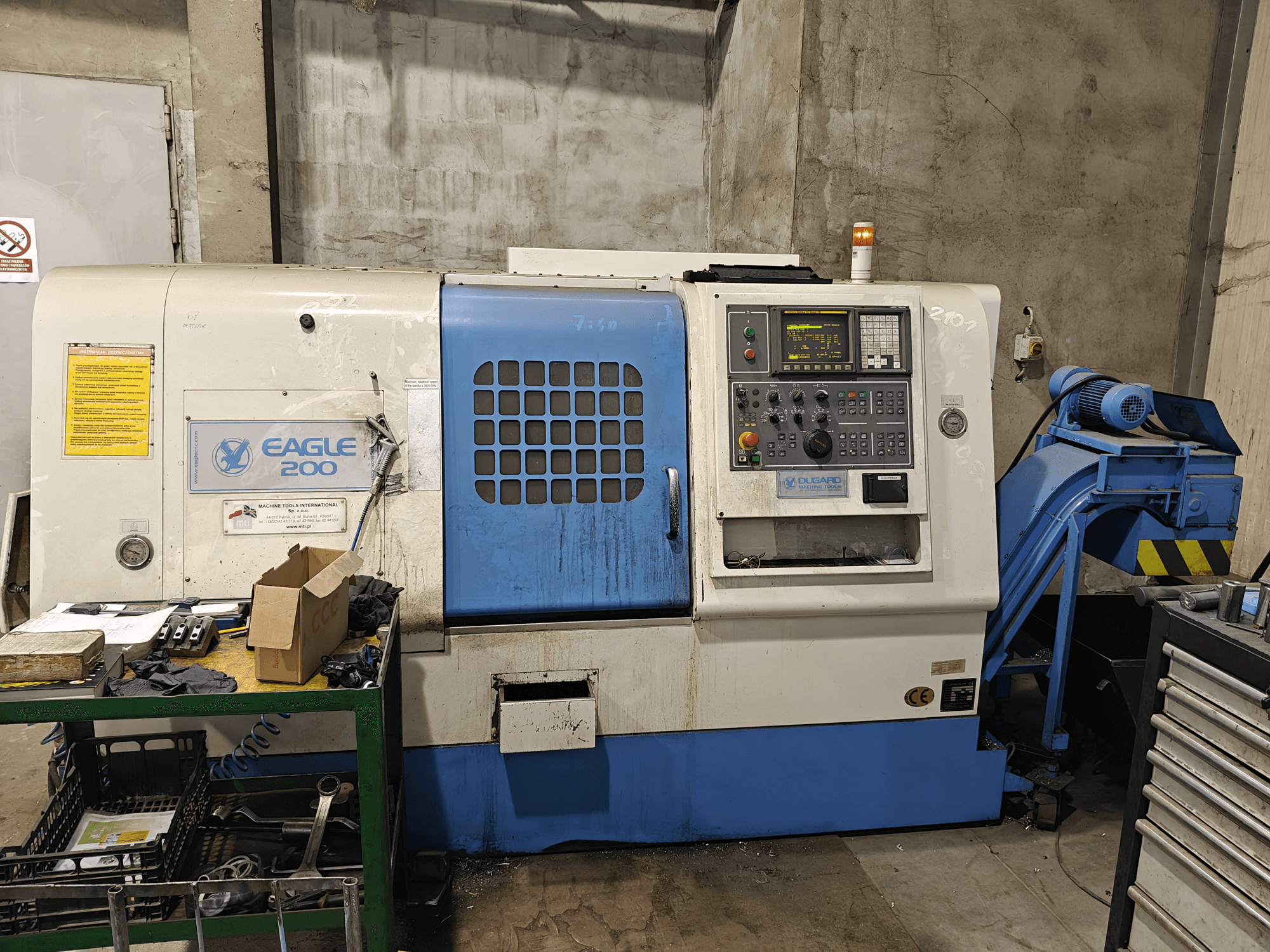 CNC stroj Eagle 200, prednji pogled s upravljačkom pločom, razni alati na zelenim kolicima. Vidljiva svjetla za habanje i rad.
