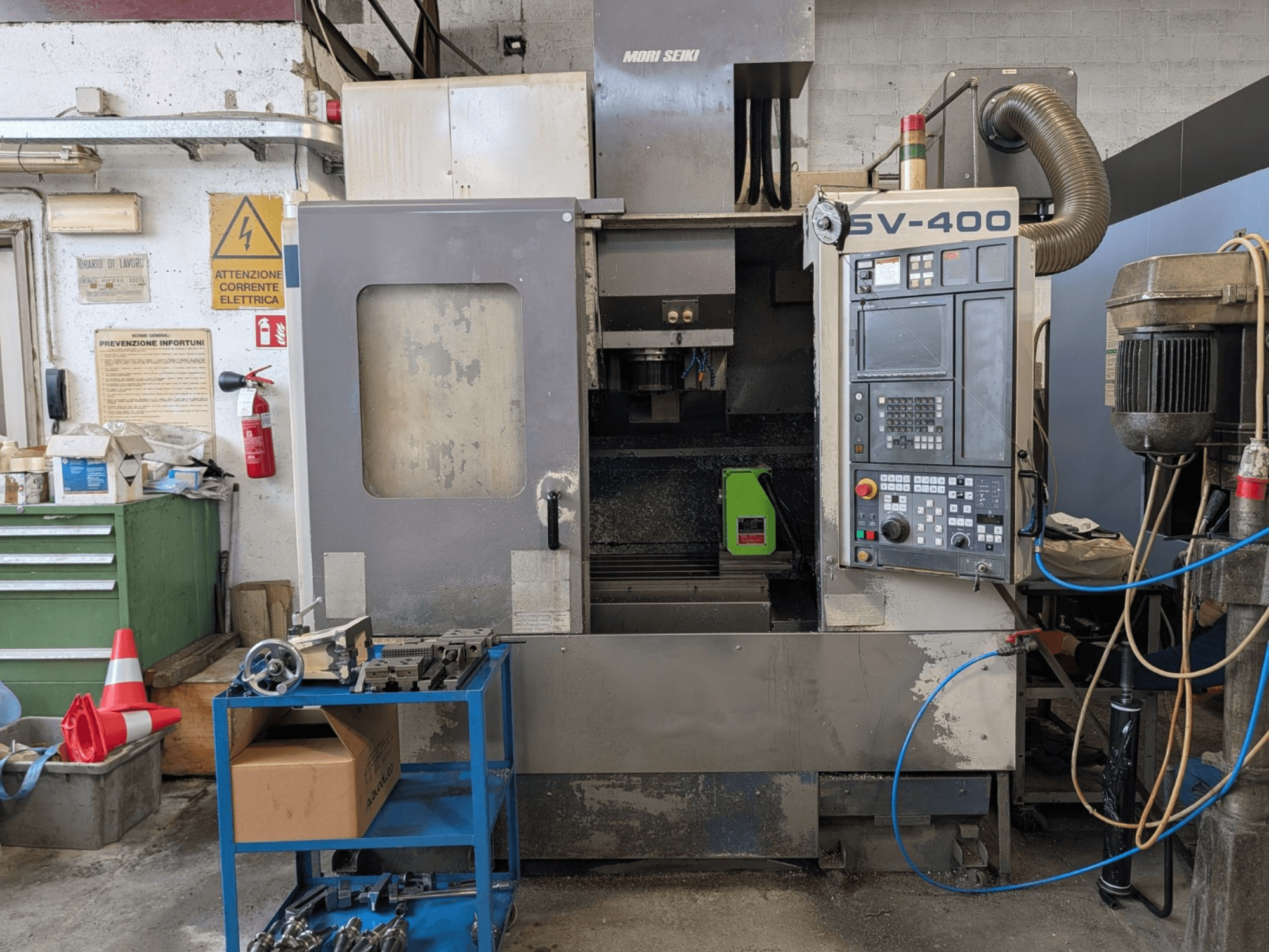 Vertikalni obradni centar MORI SEIKI SV-400 u radionici, bočni pogled, s prikazom upravljačke ploče i alatnih strojeva u blizini.