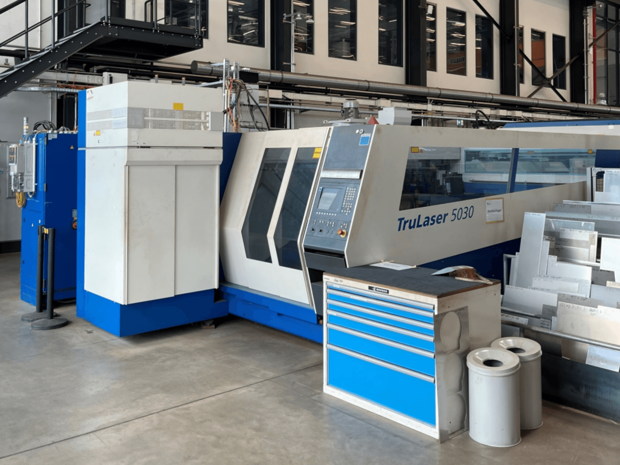 TRUMPF TruLaser 5030 CO2 laserski stroj za rezanje u prednjem pogledu, s upravljačkom pločom i obližnjim radnim stolom s metalnim limovima.