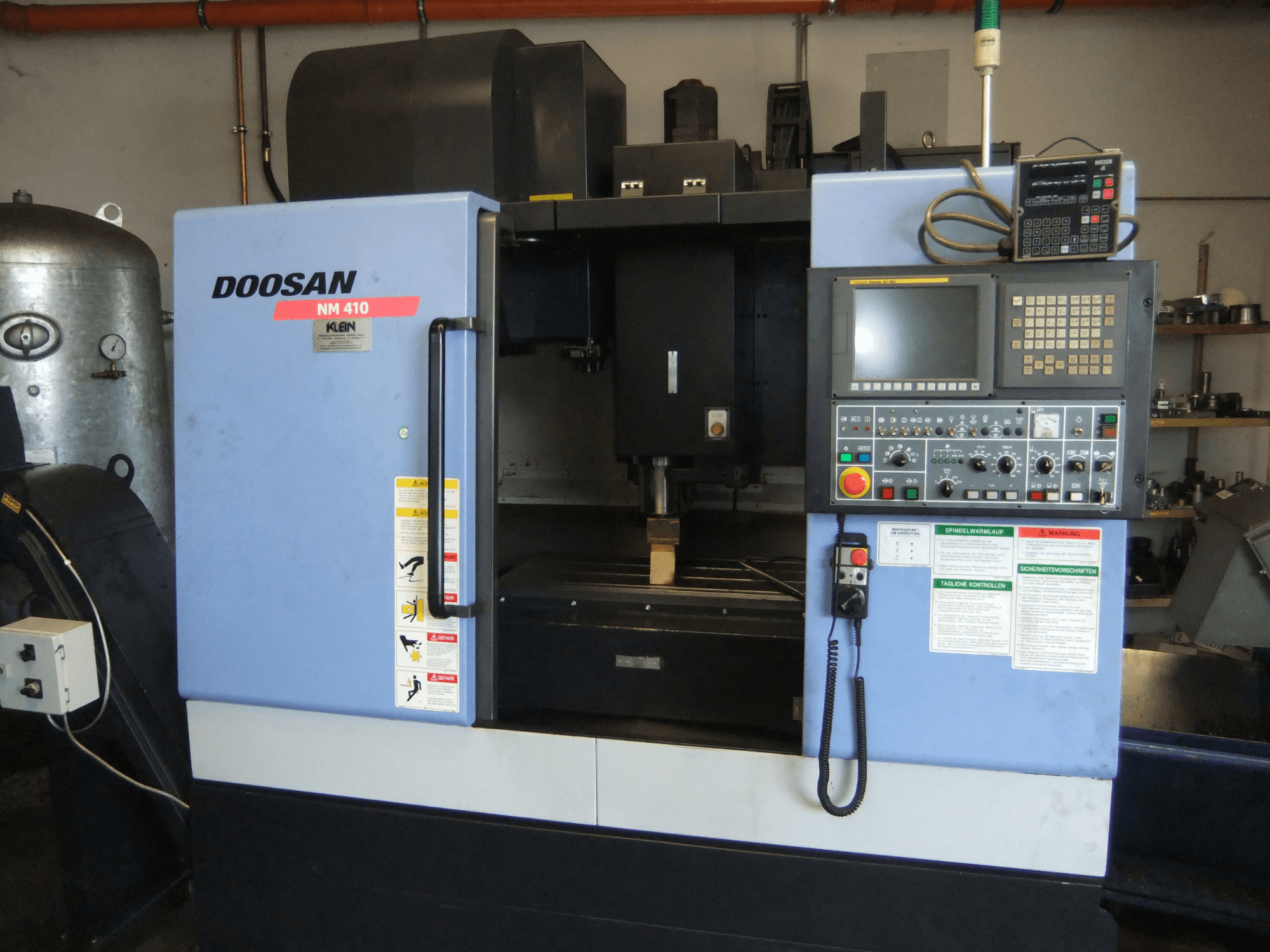 Vertikalni obradni centar DOOSAN NM 410, prednji pogled, prikaz upravljačke ploče, područja vretena i sigurnosnih naljepnica.