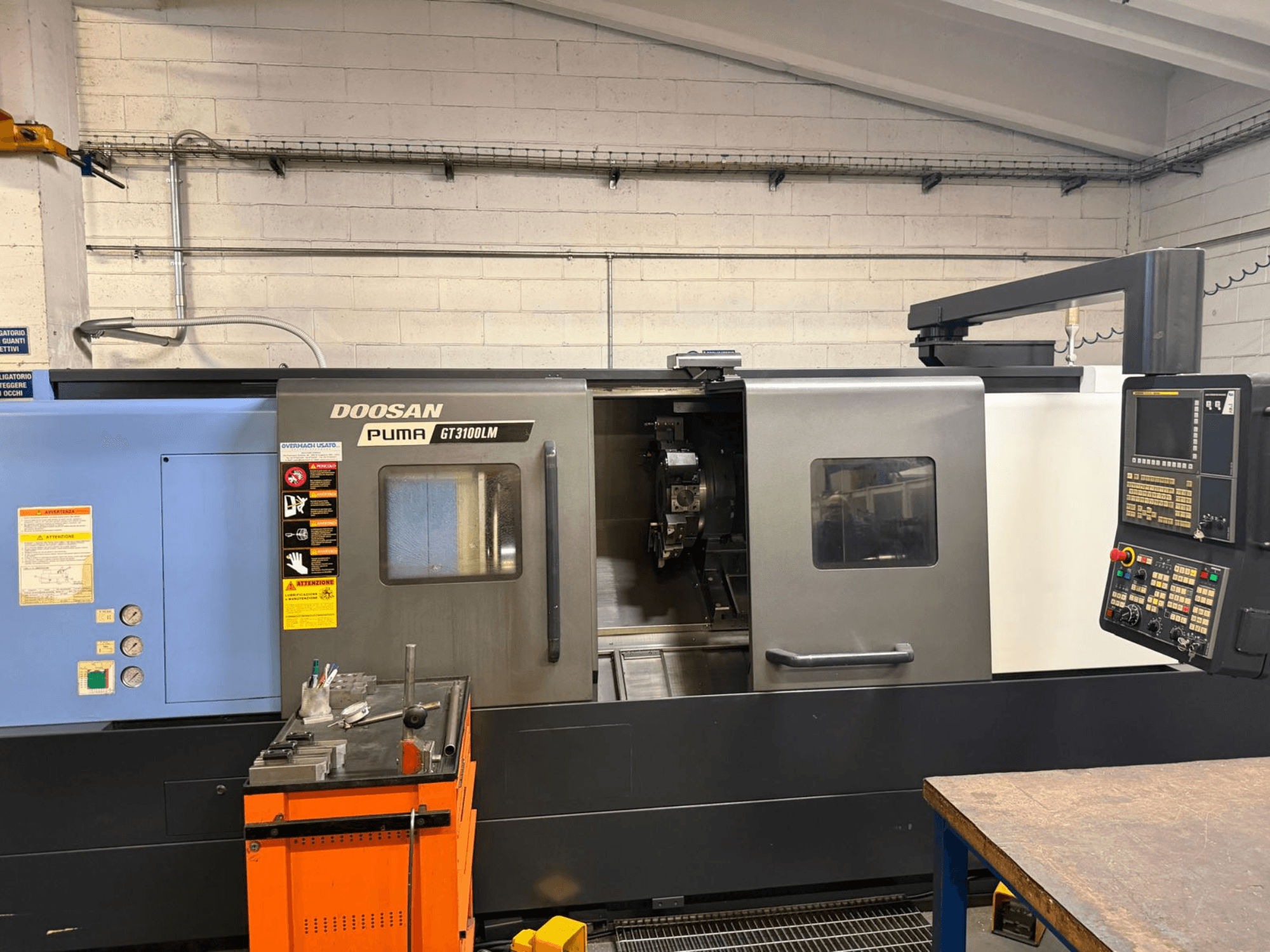 Prednji pogled na horizontalni tokarski stroj DOOSAN PUMA GT3100LM, s prikazom upravljačke ploče i radnog prostora s alatima.