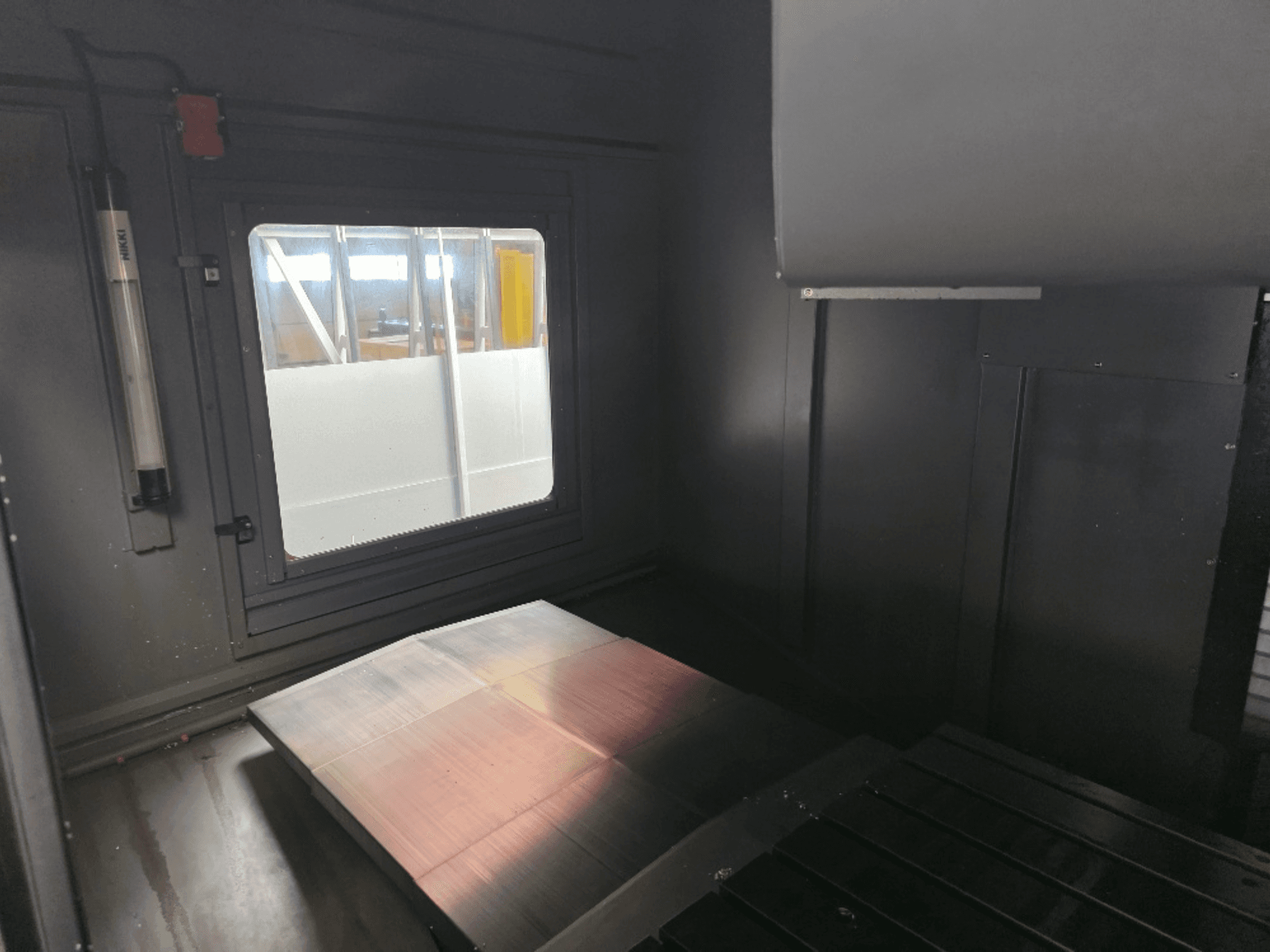 Unutarnji pogled na kućište stroja s poliranom metalnom pločom, bočnim prozorom i minimalnim osvjetljenjem. Nije vidljiva marka.