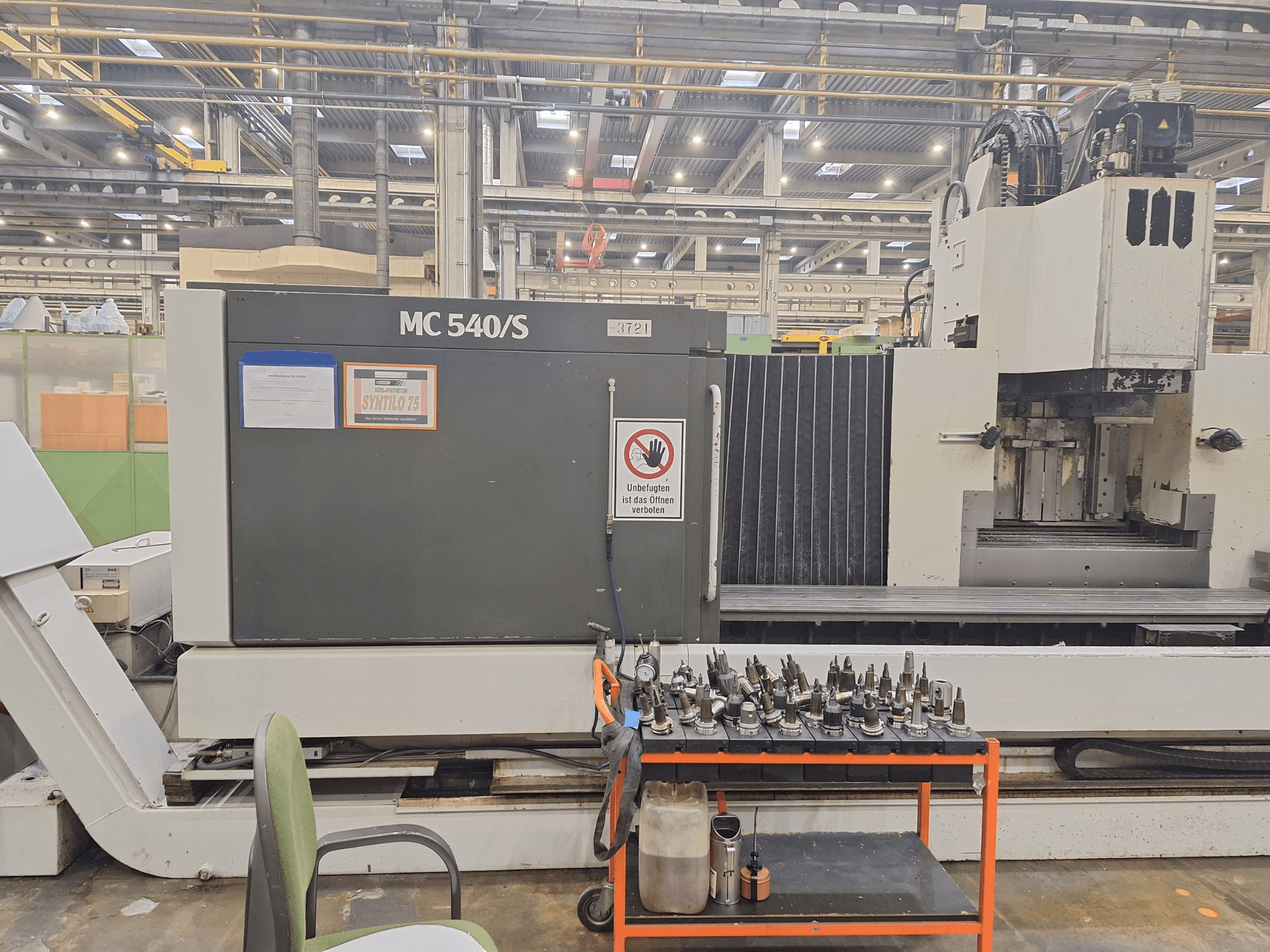 Vertikalni obradni centar STAMA MC 540S u radionici, bočni pogled s držačima alata na kolicima u blizini.