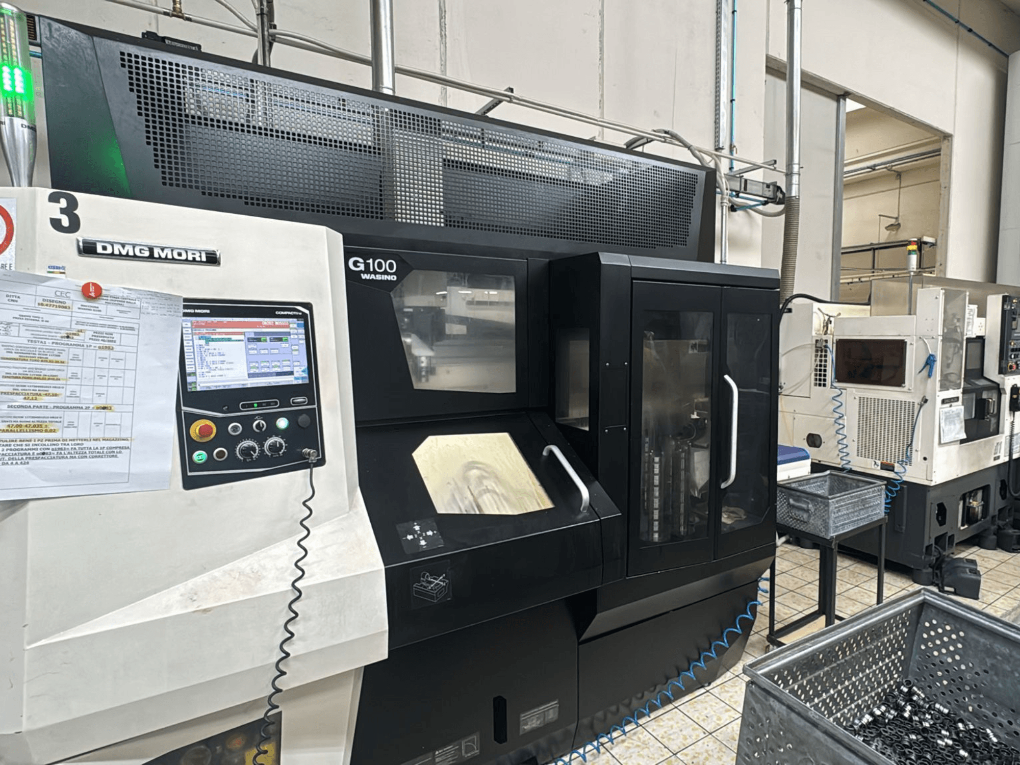 Stroj DMG MORI G100 u tvornici, prednji pogled, s digitalnom upravljačkom pločom i obližnjim spremnicima za alate.