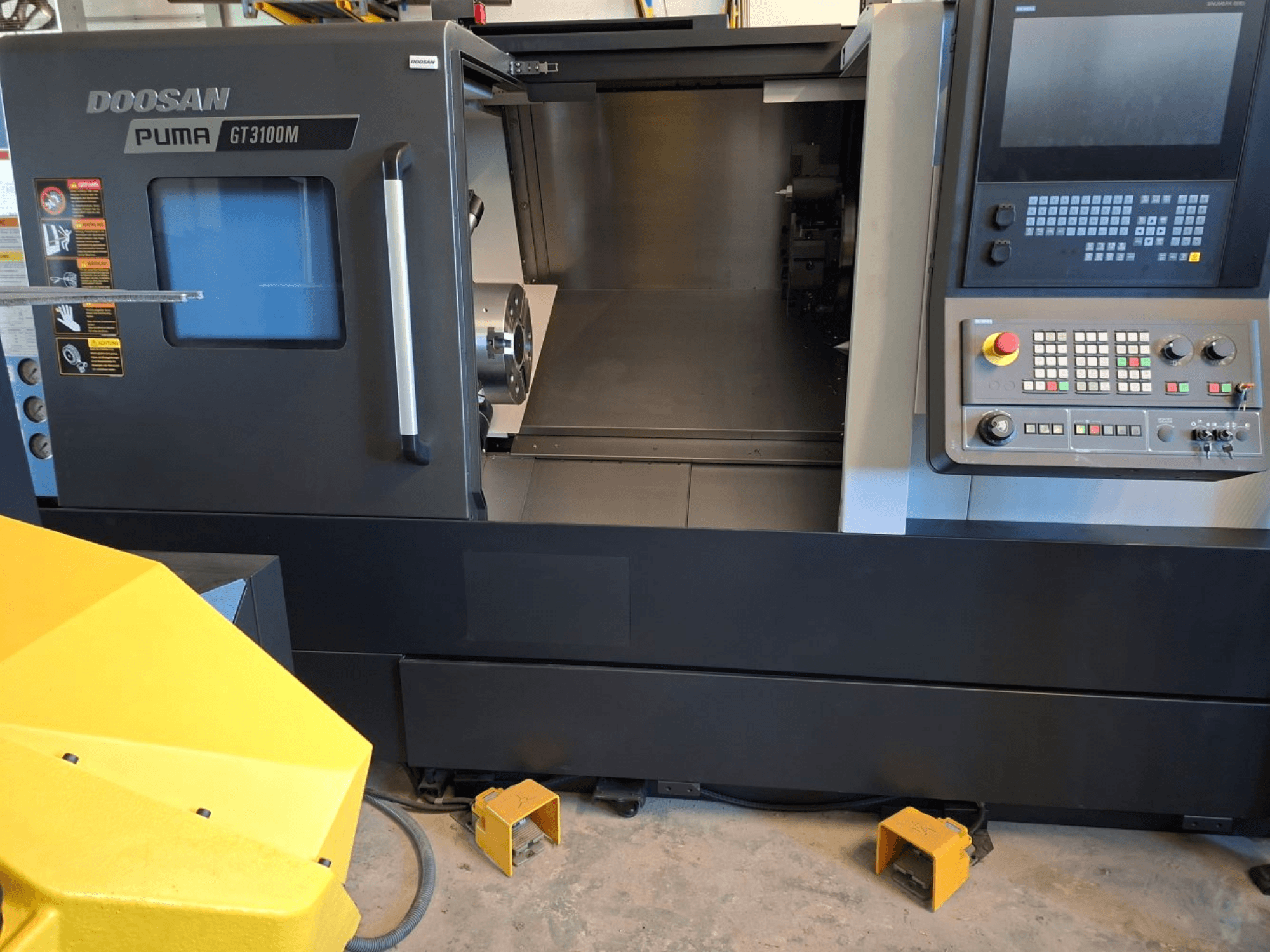 Horizontalni tokarski stroj DOOSAN Puma GT 3100 M u prednjem pogledu, s prikazom upravljačke ploče, otvorene kupole i unutarnjeg radnog prostora.