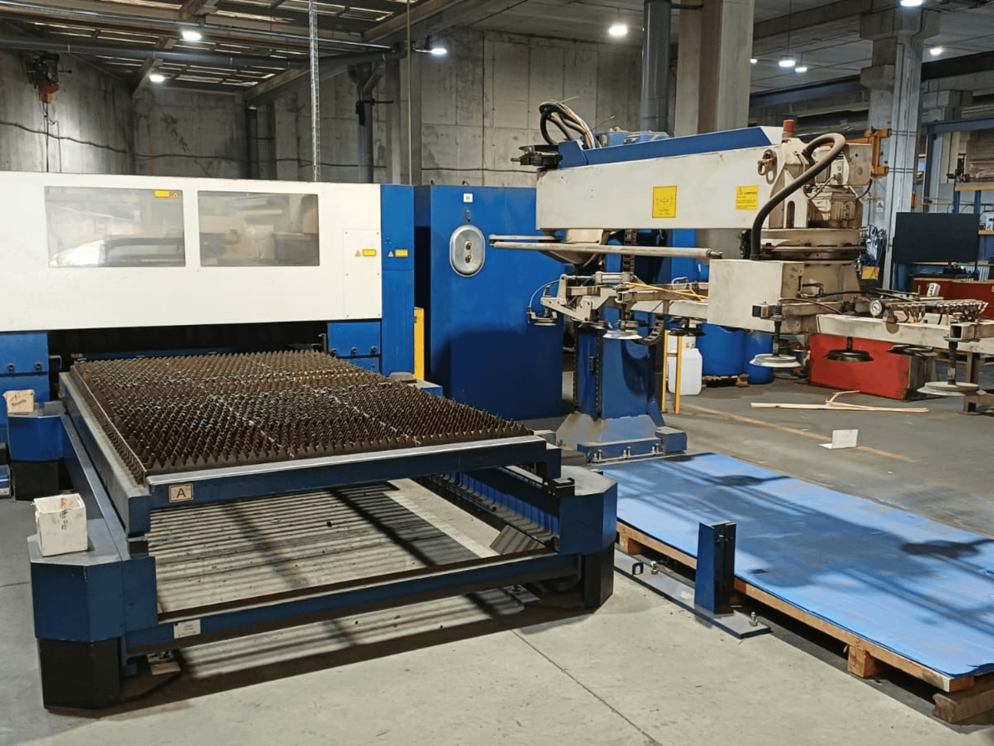 TRUMPF TRUMATIC L 3030 CO2 laserski stroj za rezanje, bočni pogled, prikazuje stol za rezanje s nazubljenom površinom i robotsku ruku.