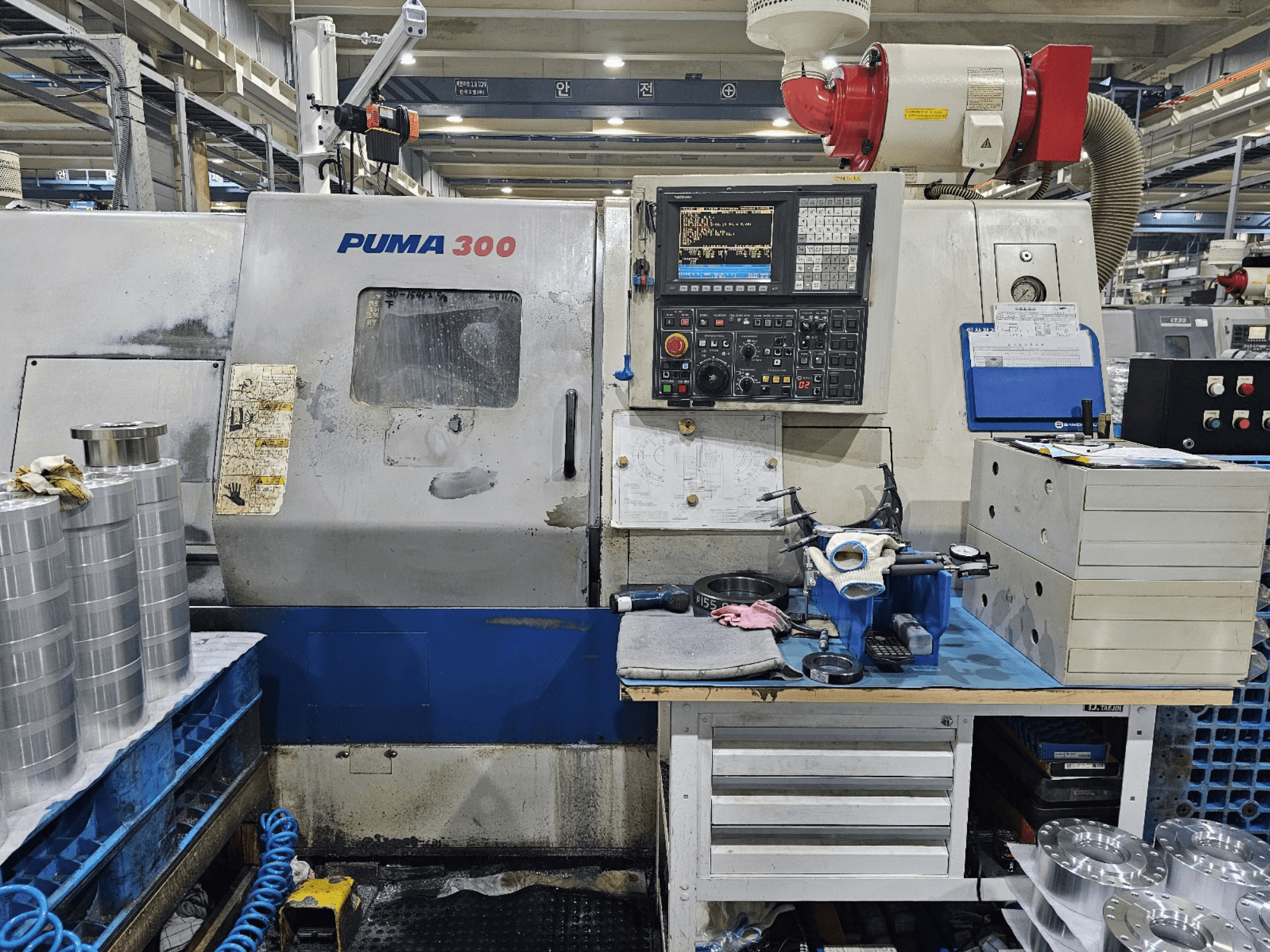 CNC stroj PUMA 300 u radionici; prednji pogled koji prikazuje upravljačku ploču, alate i metalne dijelove na radnom stolu.