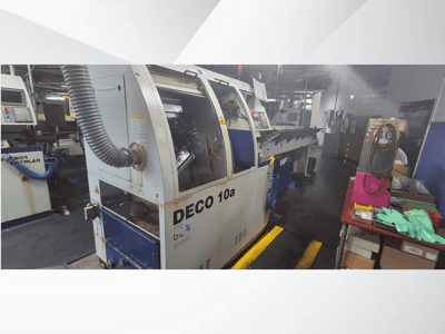 DECO 10a CNC stroj u radionici, pogled sprijeda; ima upravljačku ploču i sustav za usisavanje prašine, s radnim stolom u blizini.