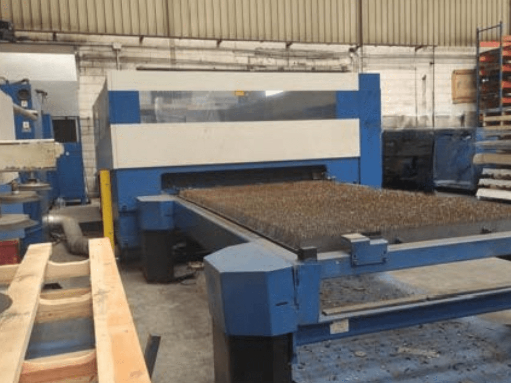 Plavi laserski stroj za rezanje s teksturiranim metalnim krevetom, bočni pogled, prikazuje operativnu postavku u industrijskom radnom prostoru.