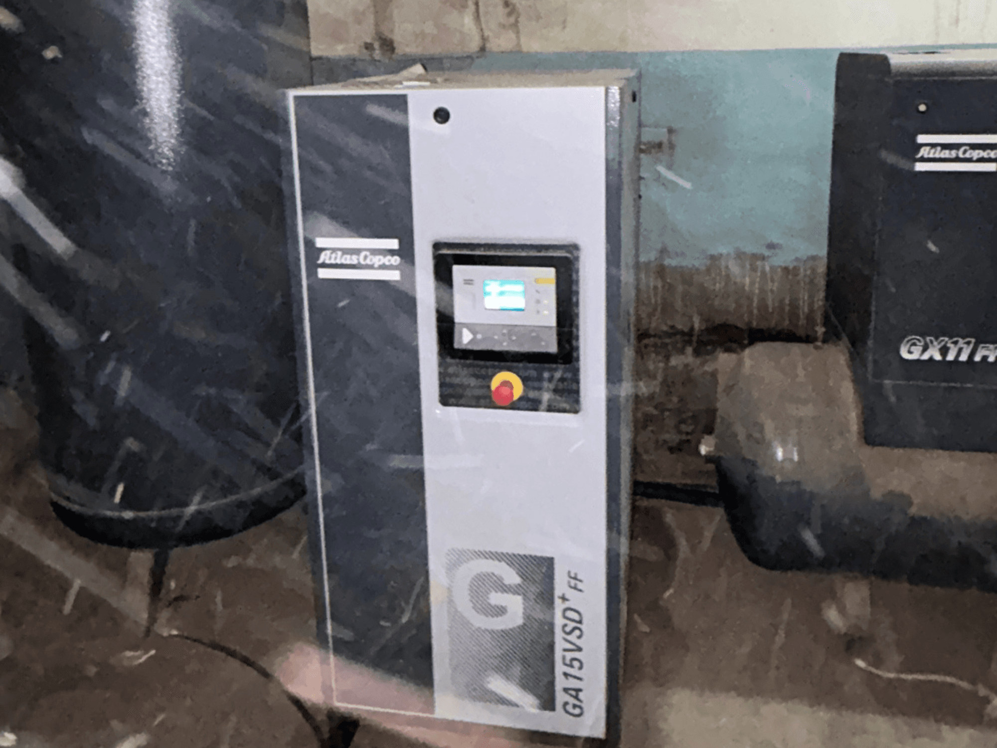 Zračni kompresor Atlas Copco GA15VSD+FF, pogled sprijeda, uključuje upravljačku ploču sa zaslonom i crvenim gumbom za zaustavljanje u nuždi.