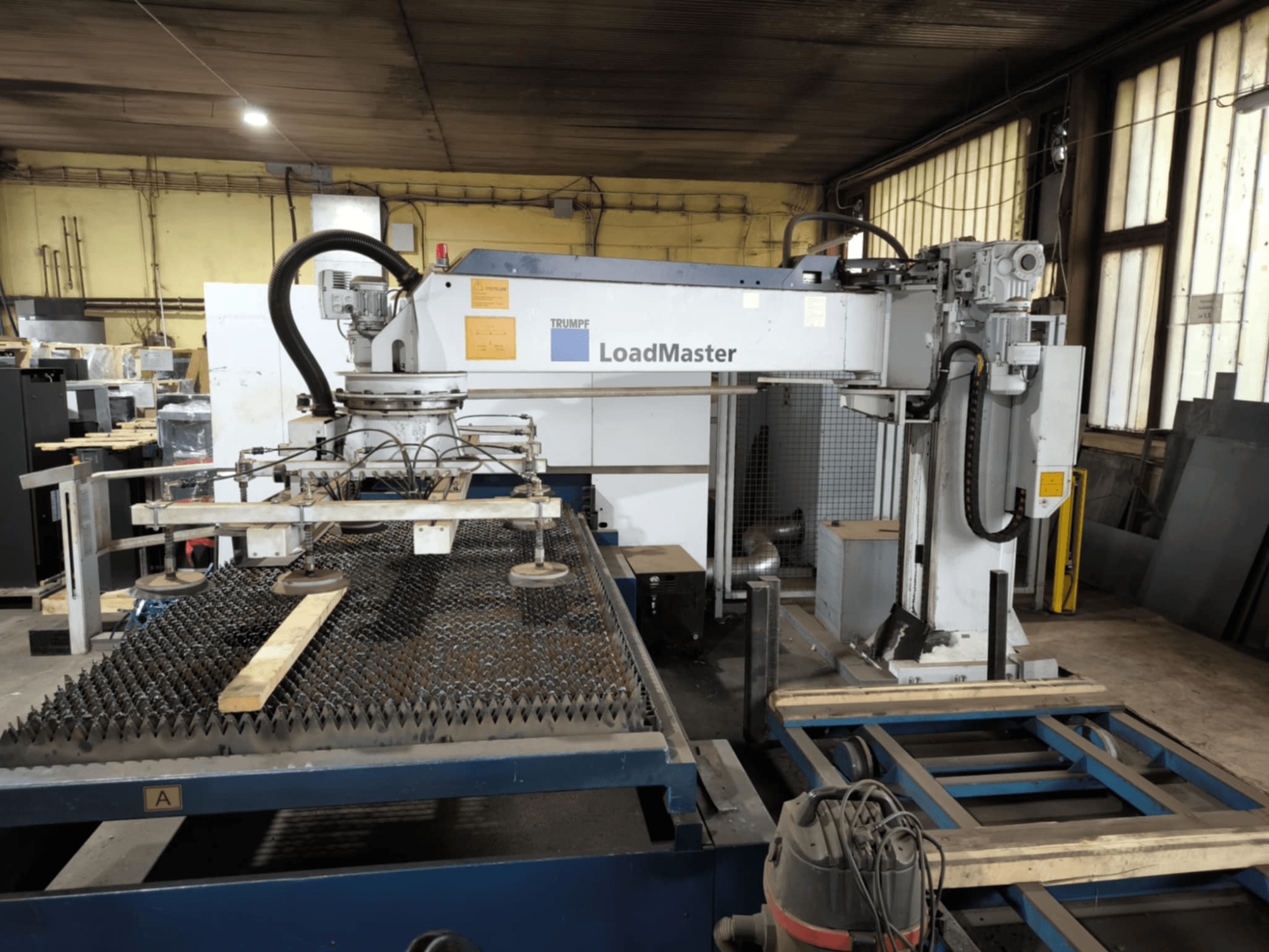 Stroj za rezanje TRUMPF TRULASER 3030 FIBER, pogled sprijeda, s prikazom LoadMaster sustava i postavljen na rešetkastom radnom stolu.