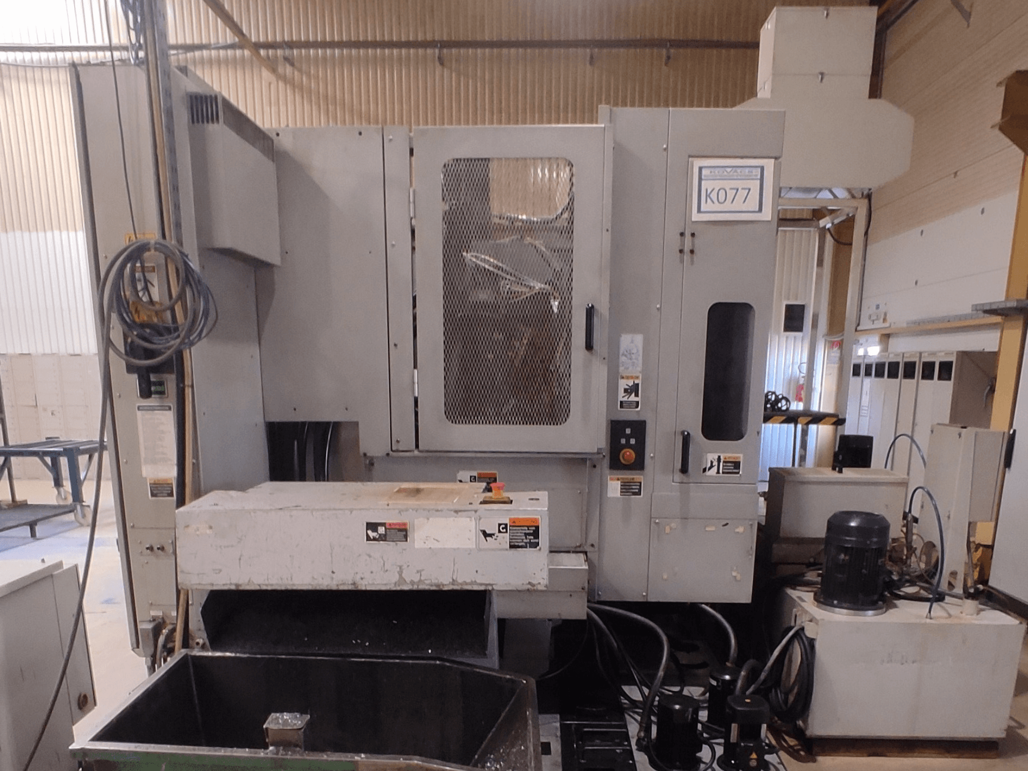 Sivi industrijski CNC stroj s velikim radnim stolom, bočni pogled, s upravljačkom pločom i spremnikom rashladne tekućine, model K077.