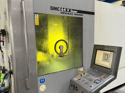 DMC 64 V linear tvrtke Deckel Maho, prednji pogled na stroj s upravljačkom pločom i žuto obojenim prozorom koji prikazuje unutarnje mehanizme.