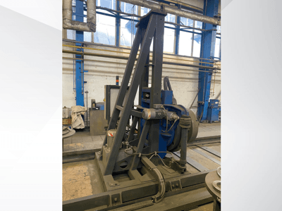 Industrijski stroj s plavim motorom i metalnim okvirom, gledan sprijeda u radioničkom okruženju.