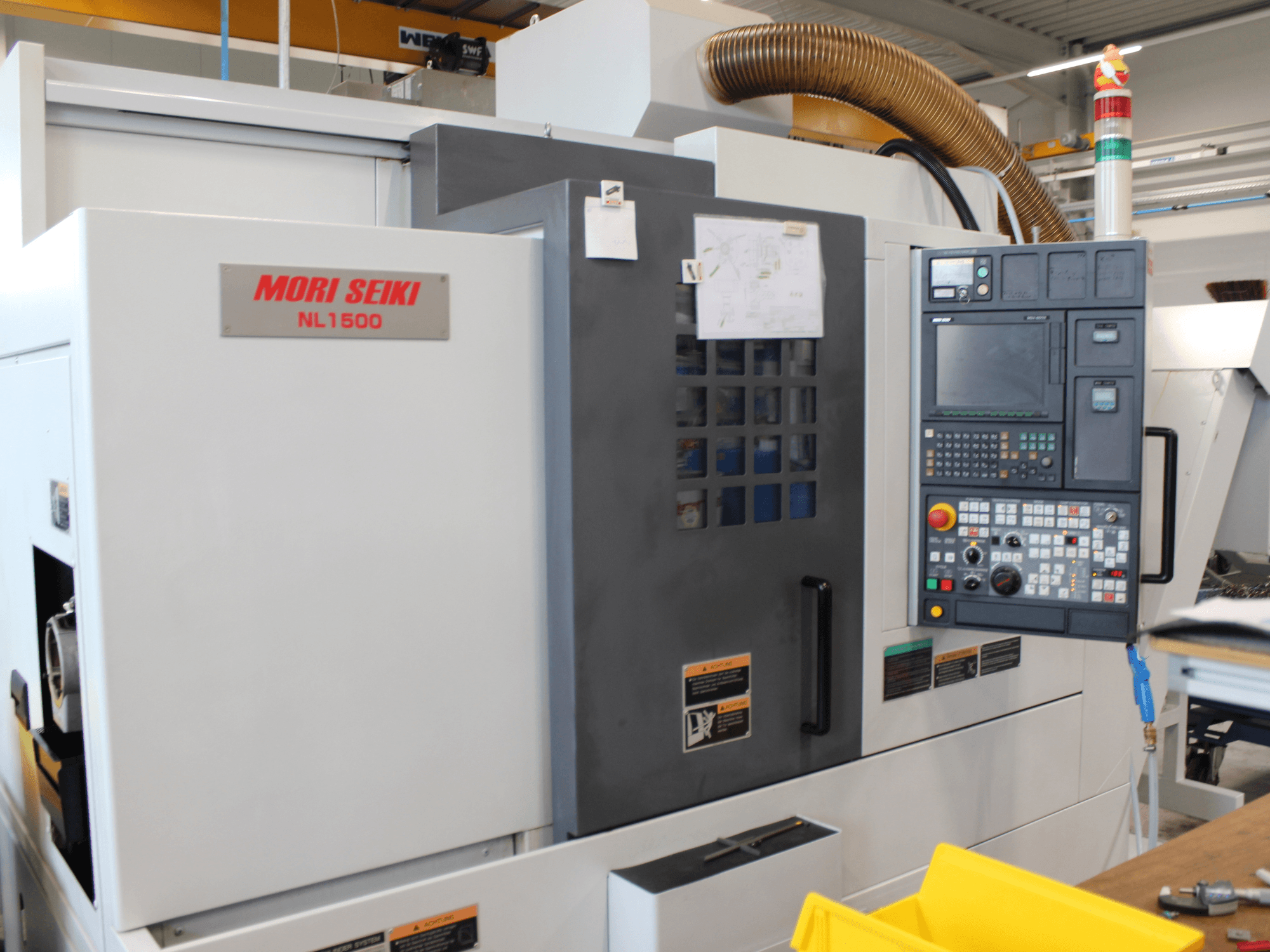 MORI SEIKI NL 1500 SY tokarsko-glodački centar u bočnom pogledu, s upravljačkom pločom, naljepnicama o sigurnosti rada i sustavom hlađenja.