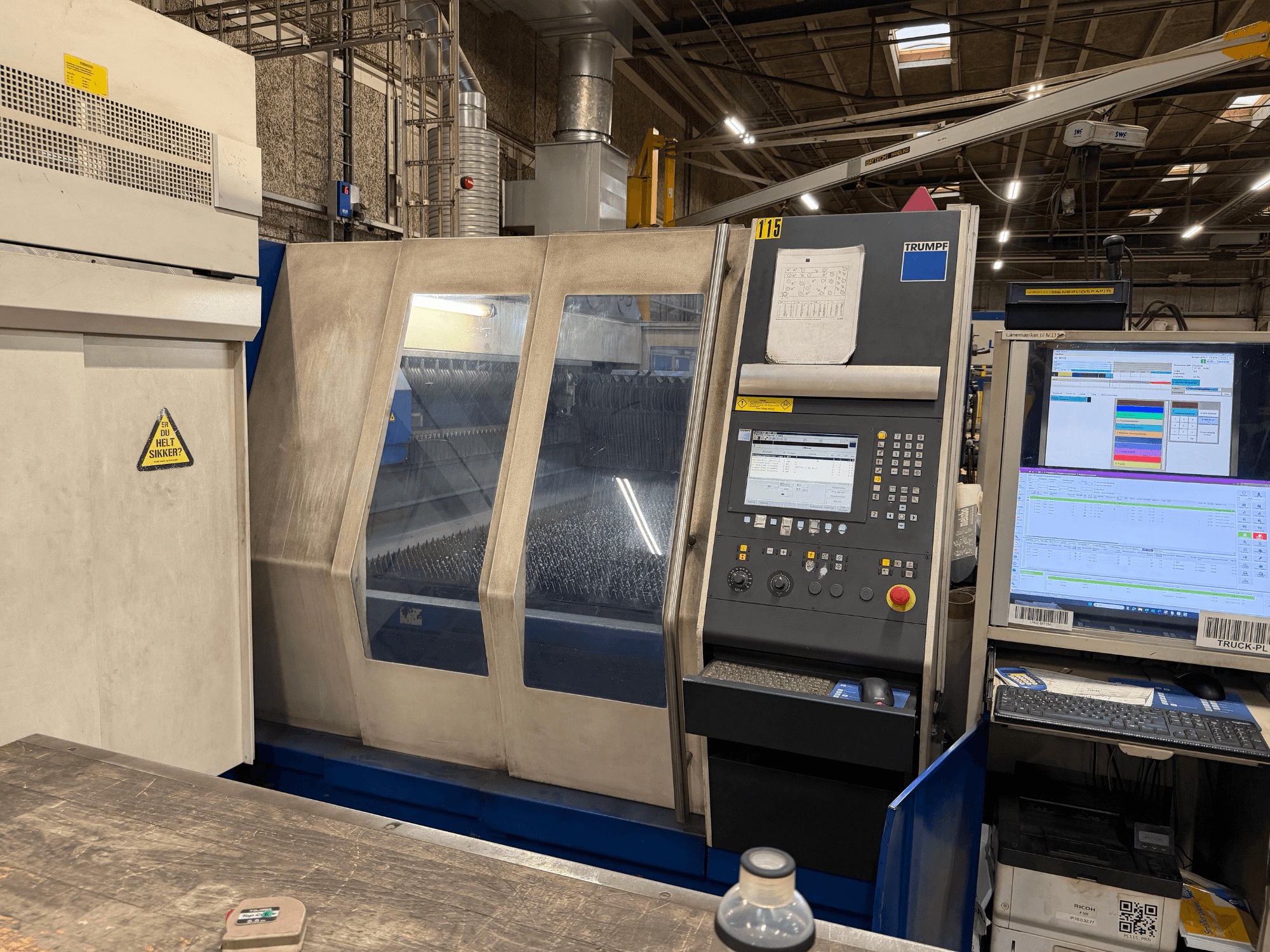Prednji pogled na Trumpf industrijski laserski stroj s upravljačkom pločom i digitalnim zaslonima, smješten u tvorničkom okruženju.