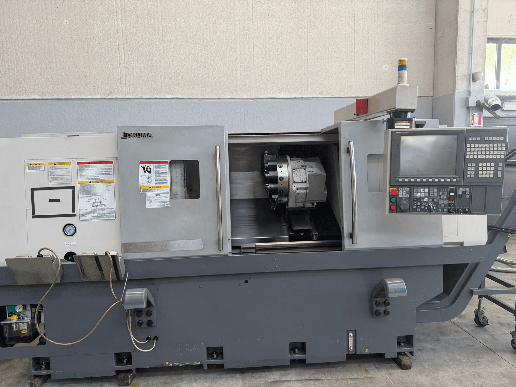 Okuma CNC tokarski stroj, prednji pogled, prikazuje upravljačku ploču, držač alata za rezanje i sigurnosna upozorenja sa strane.