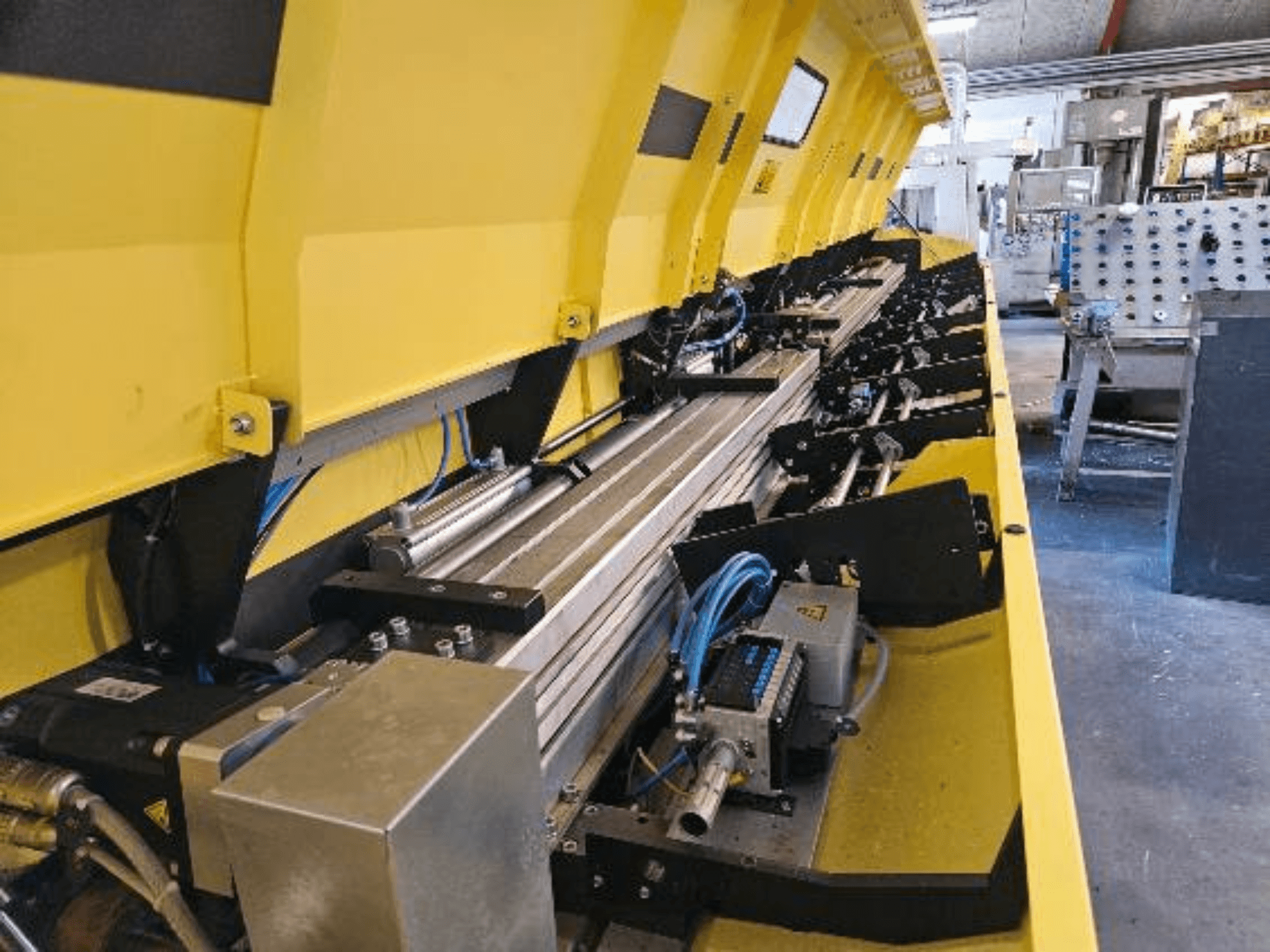 Pogled izbliza na žuti hidraulički stroj s metalnim komponentama i transportnim tračnicama, s crijevima i elektroničkim dijelovima.