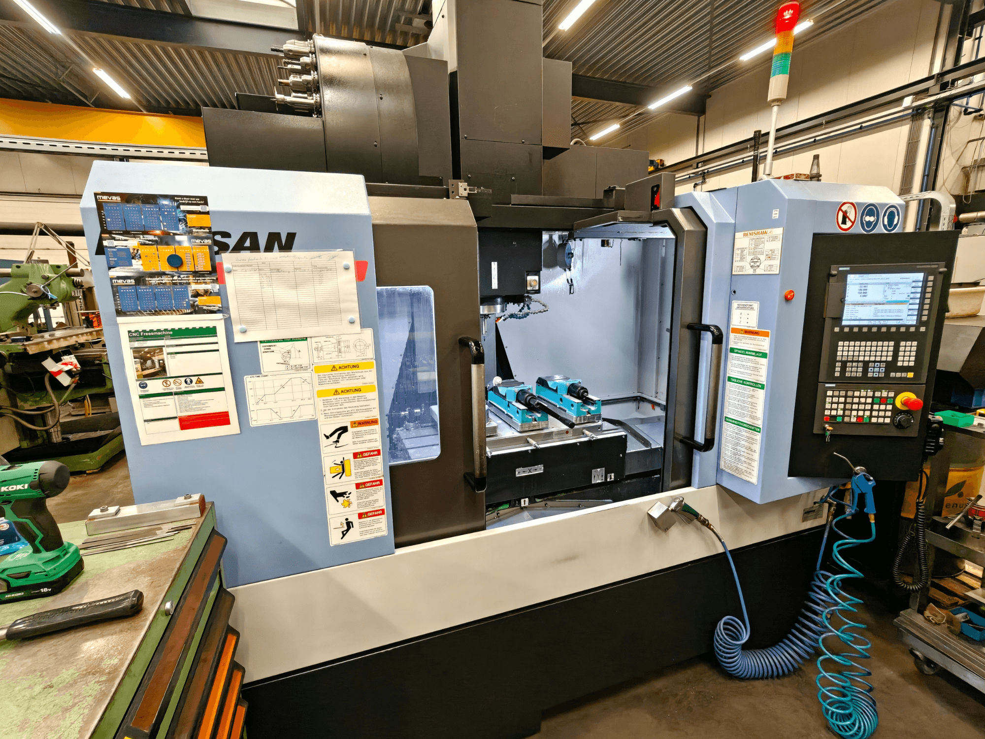 Vertikalni obradni centar DOOSAN DNM 400 II u radionici, s upravljačkim elementima, držačima alata i sigurnosnim znakovima, pogled sprijeda.
