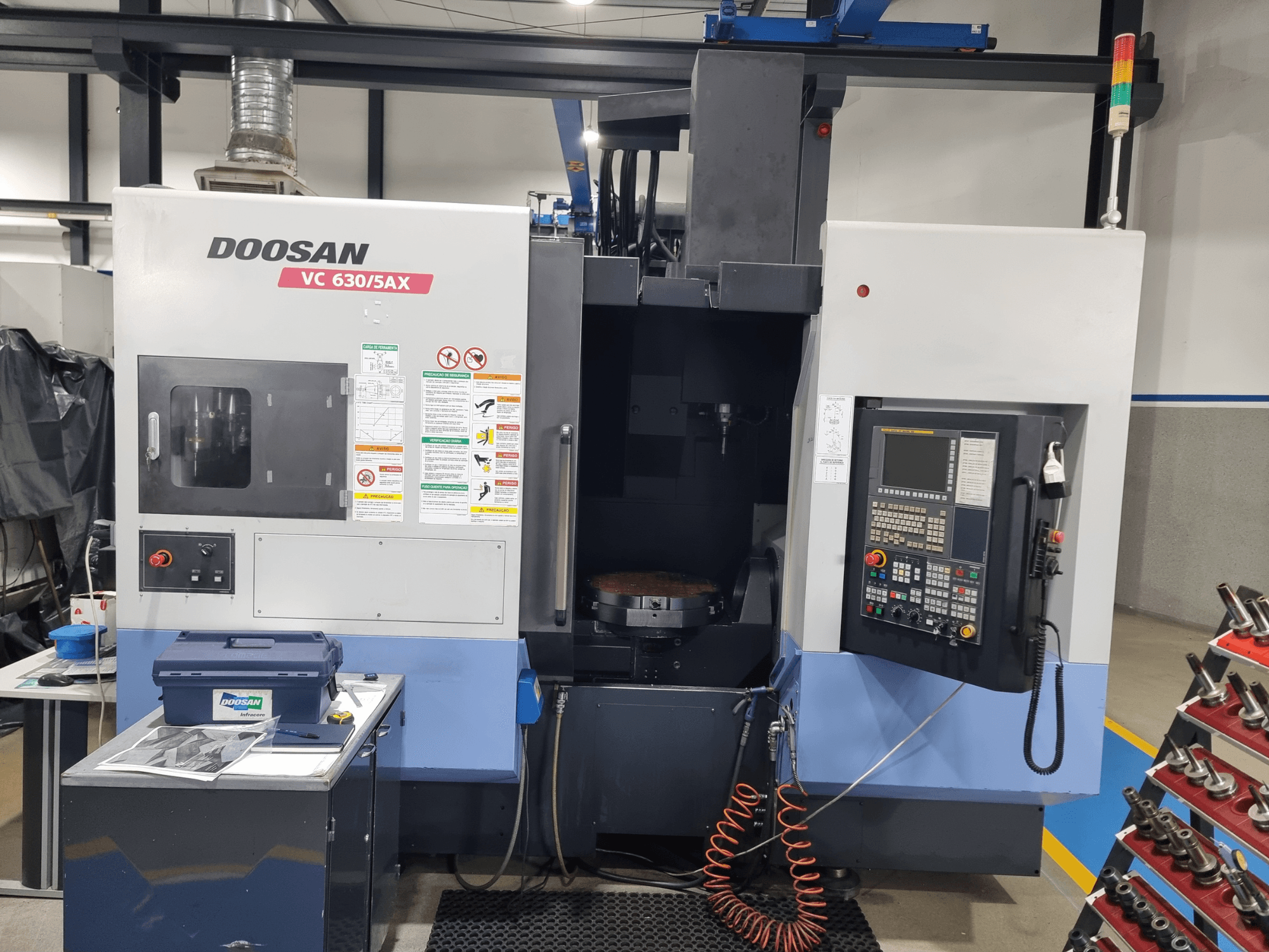 Univerzalni obradni centar DOOSAN VC 630/5AX, prednji pogled s prikazom upravljačke ploče, područja rezanja i sigurnosnih značajki.