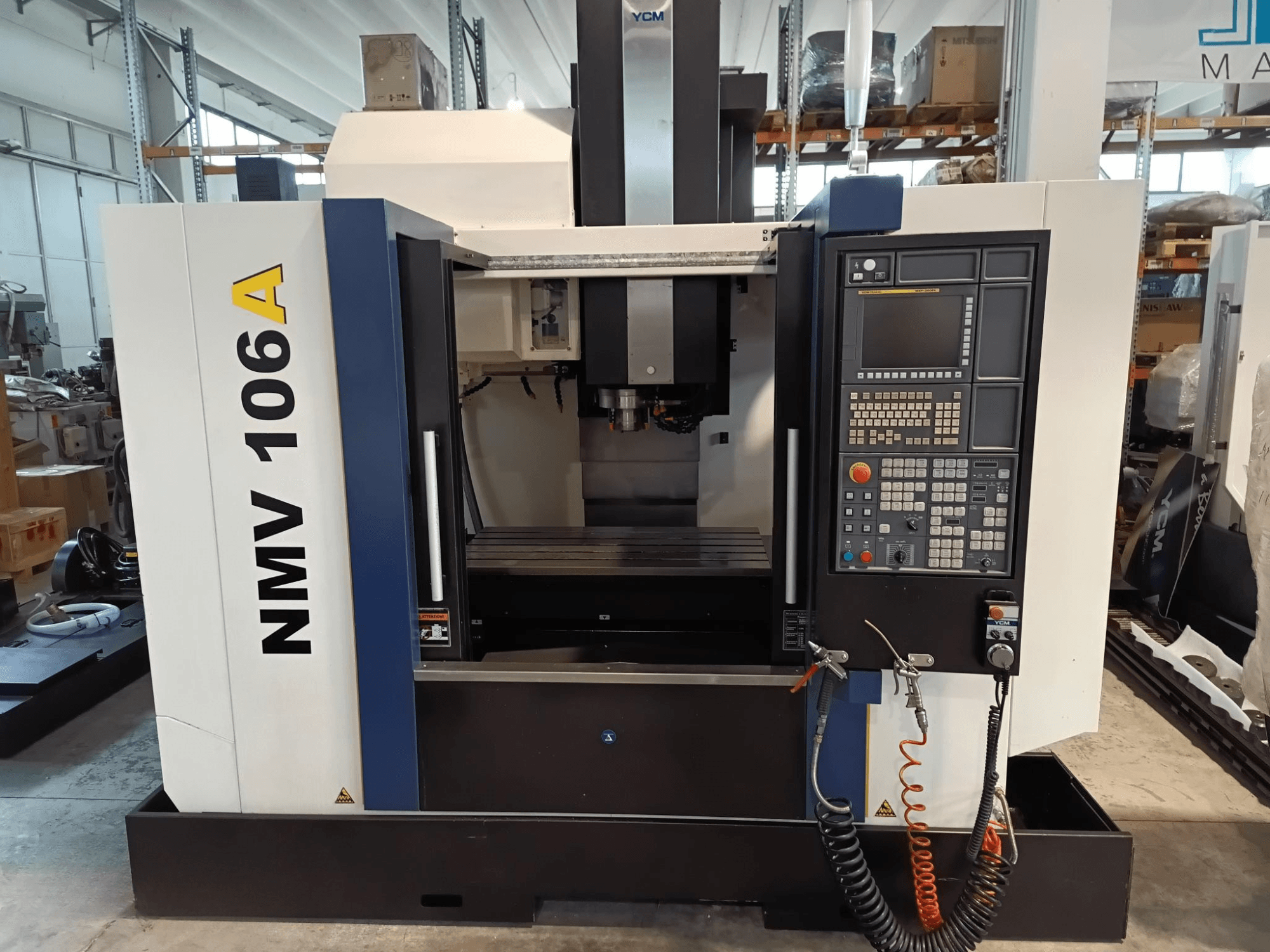 Obradni centar YCM NMV 106A, prednji pogled, s upravljačkom pločom s gumbima i crijevima za rashladnu tekućinu.