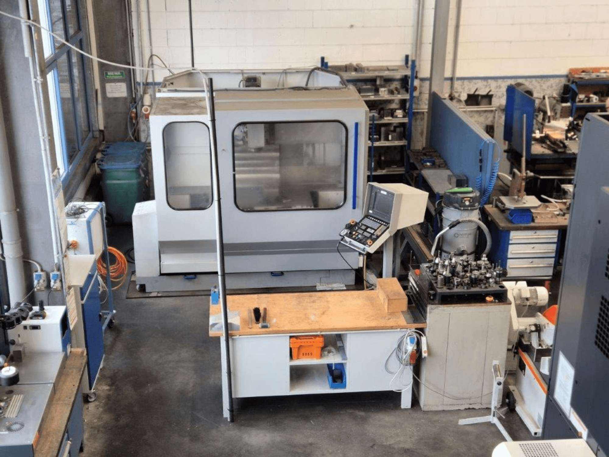 CNC glodalica u radionici, prednji pogled, s upravljačkom pločom, radnom površinom i alatima vidljivim u pozadini.