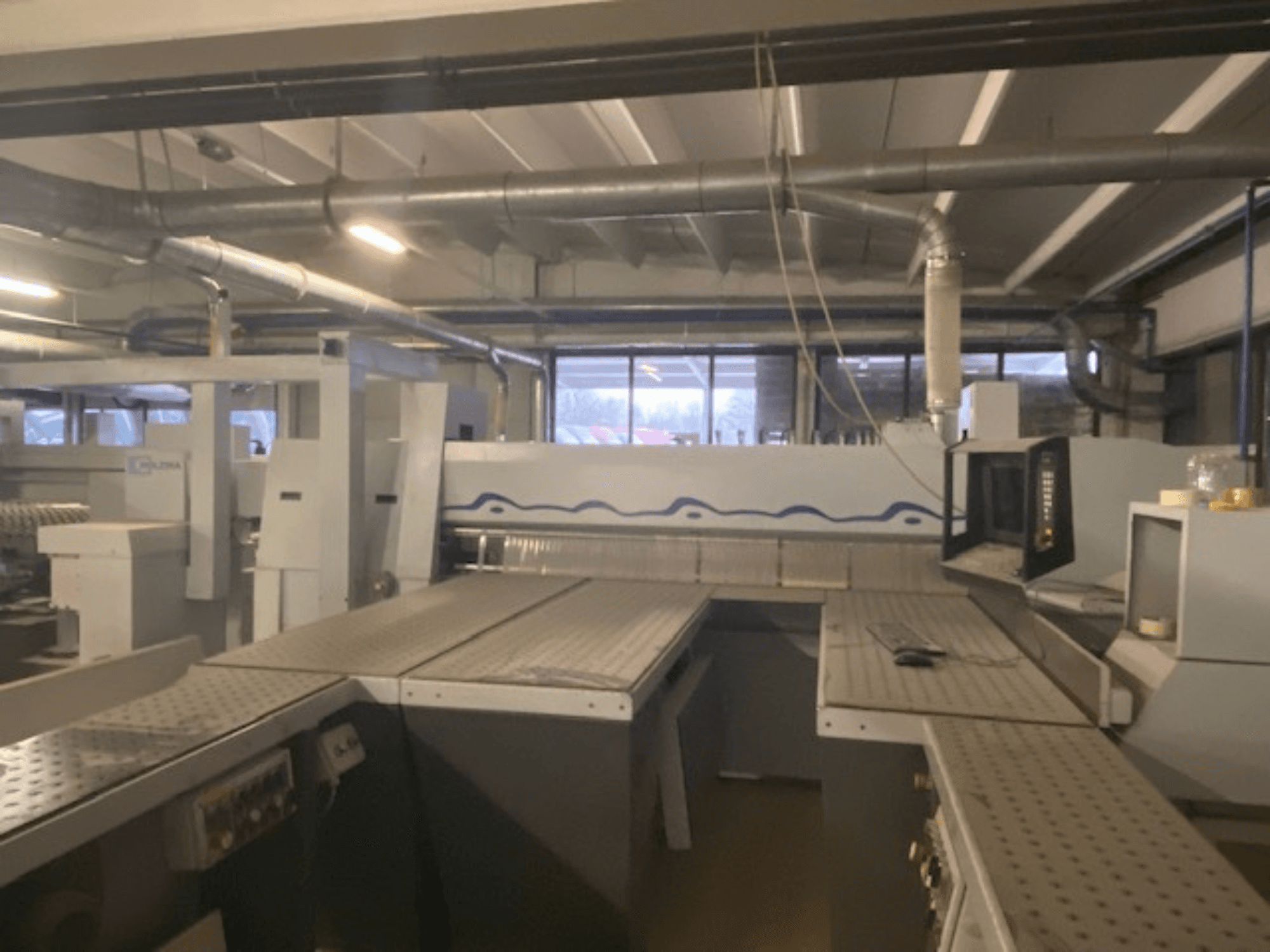 Industrijski radni prostor s postavom strojeva i upravljačkom pločom, gledano iz povišenog prednjeg kuta.