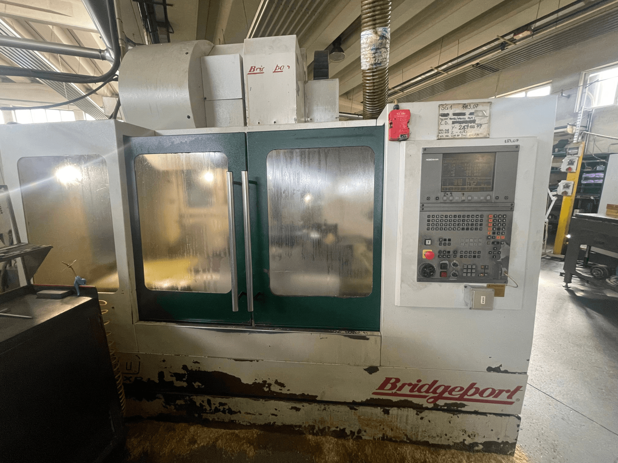 Vertikalni obradni centar Bridgeport VMC 1000/30, prednji pogled s upravljačkom pločom, na kojoj se vide istrošena vanjština i zelena vrata.