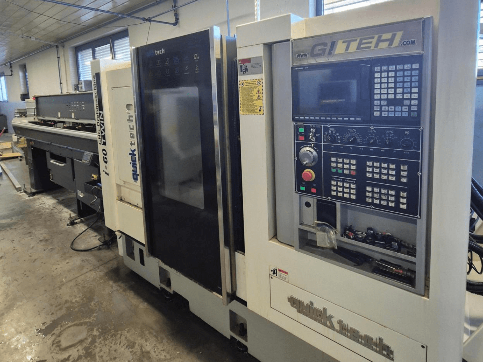 Quick Tech i-60 dvostruki CNC stroj, pogled sprijeda, s GITEH upravljačkom pločom i operativnim gumbima, u radioničkom okruženju.