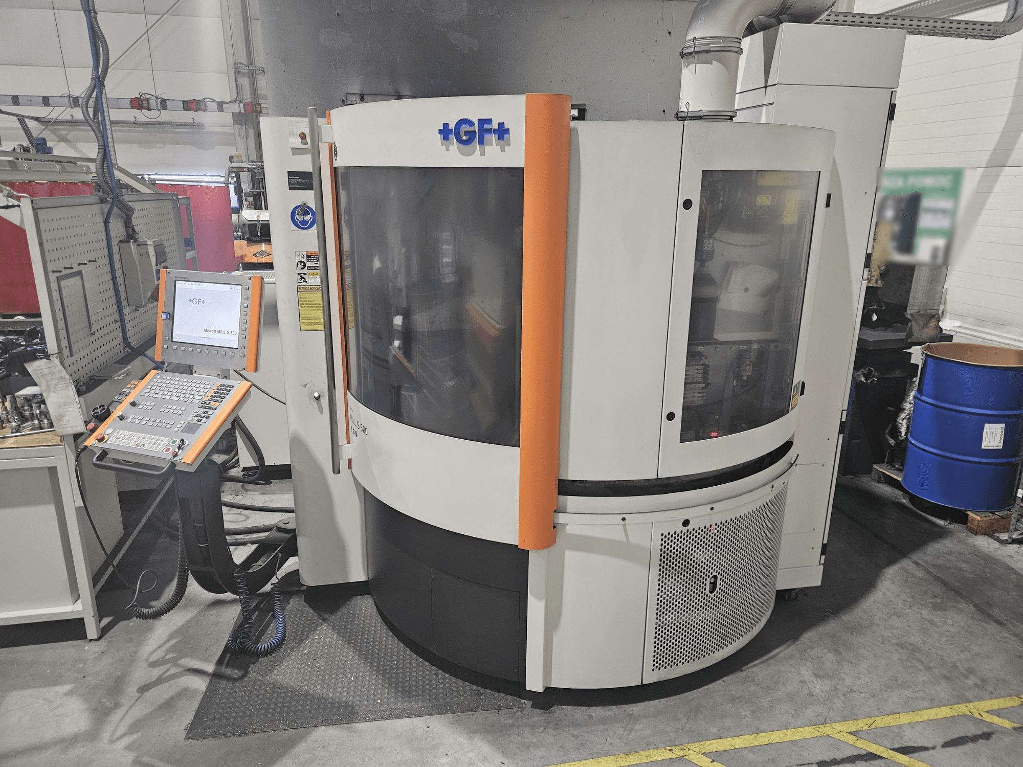 GF Machining Solutions alatni stroj s upravljačkom pločom, prednji pogled; ima prozirnu ploču, narančaste detalje i industrijski ambijent.