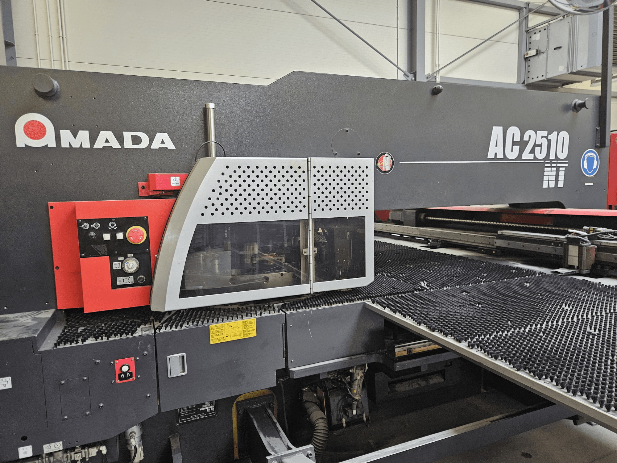 Amada AC2510 NT stroj za lasersko rezanje, prednji pogled, s upravljačkom pločom s gumbima, tipkama i sigurnosnim poklopcem.