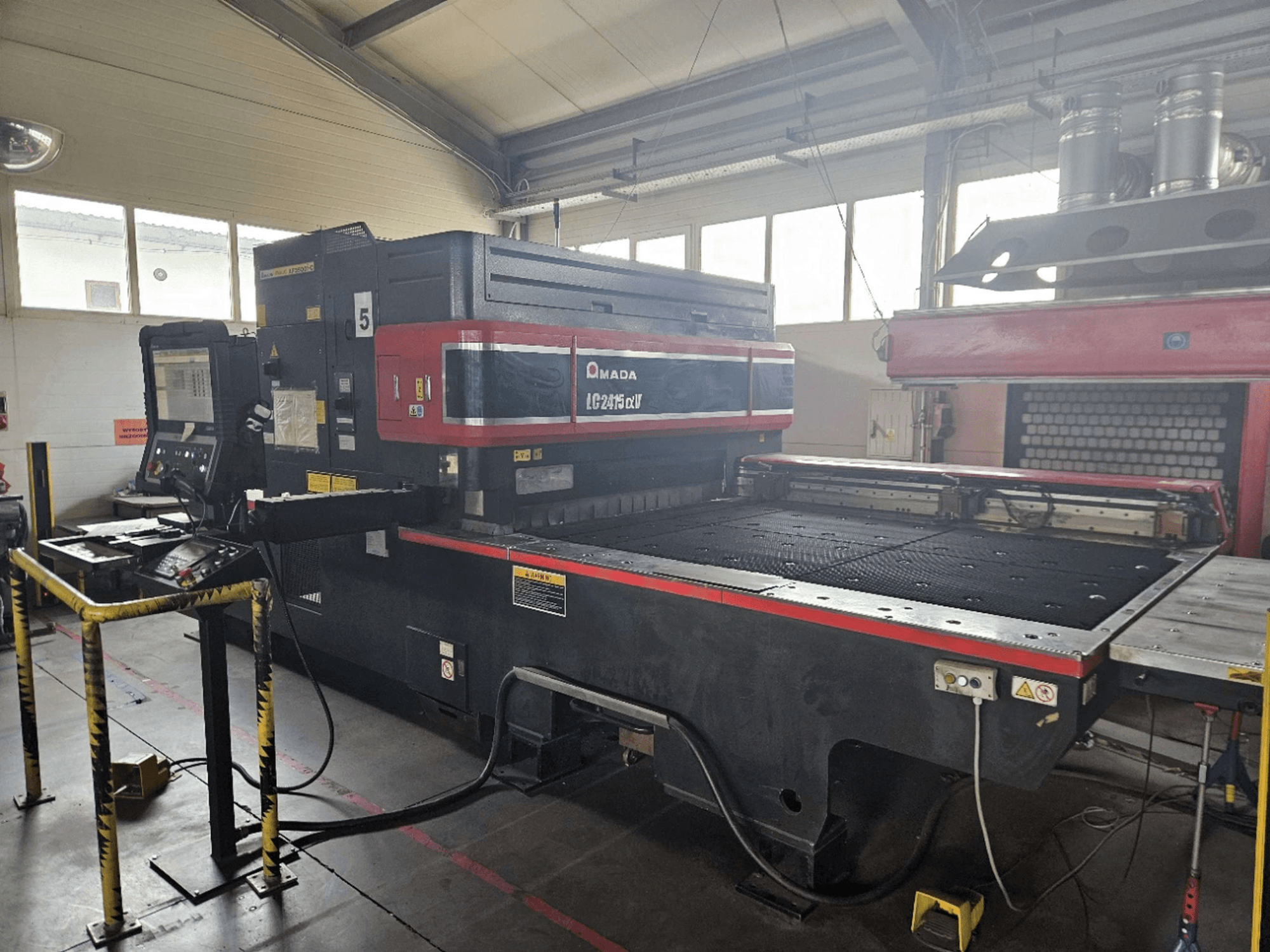 AMADA LC2415 Alpha 5 CO2 stroj za lasersko rezanje, prednji pogled s upravljačkom pločom i postoljem za rezanje sa sigurnosnim ogradama.