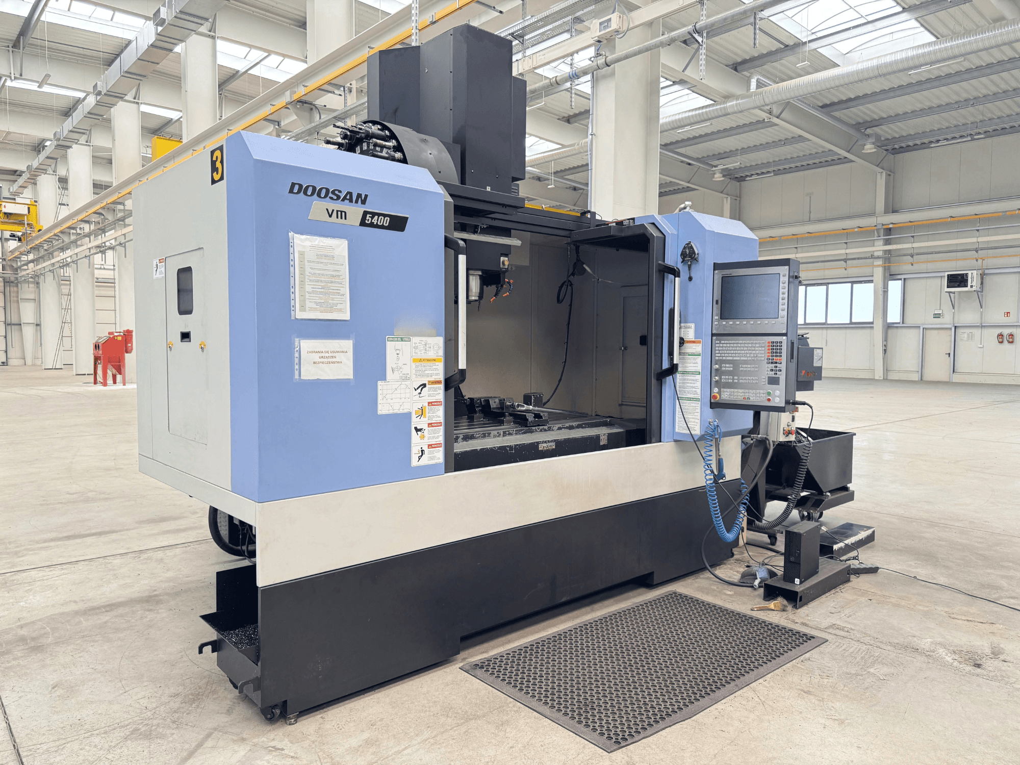 Vertikalni obradni centar DOOSAN VM 5400, prednji pogled s upravljačkom pločom i radnim prostorom u prostranom industrijskom okruženju.