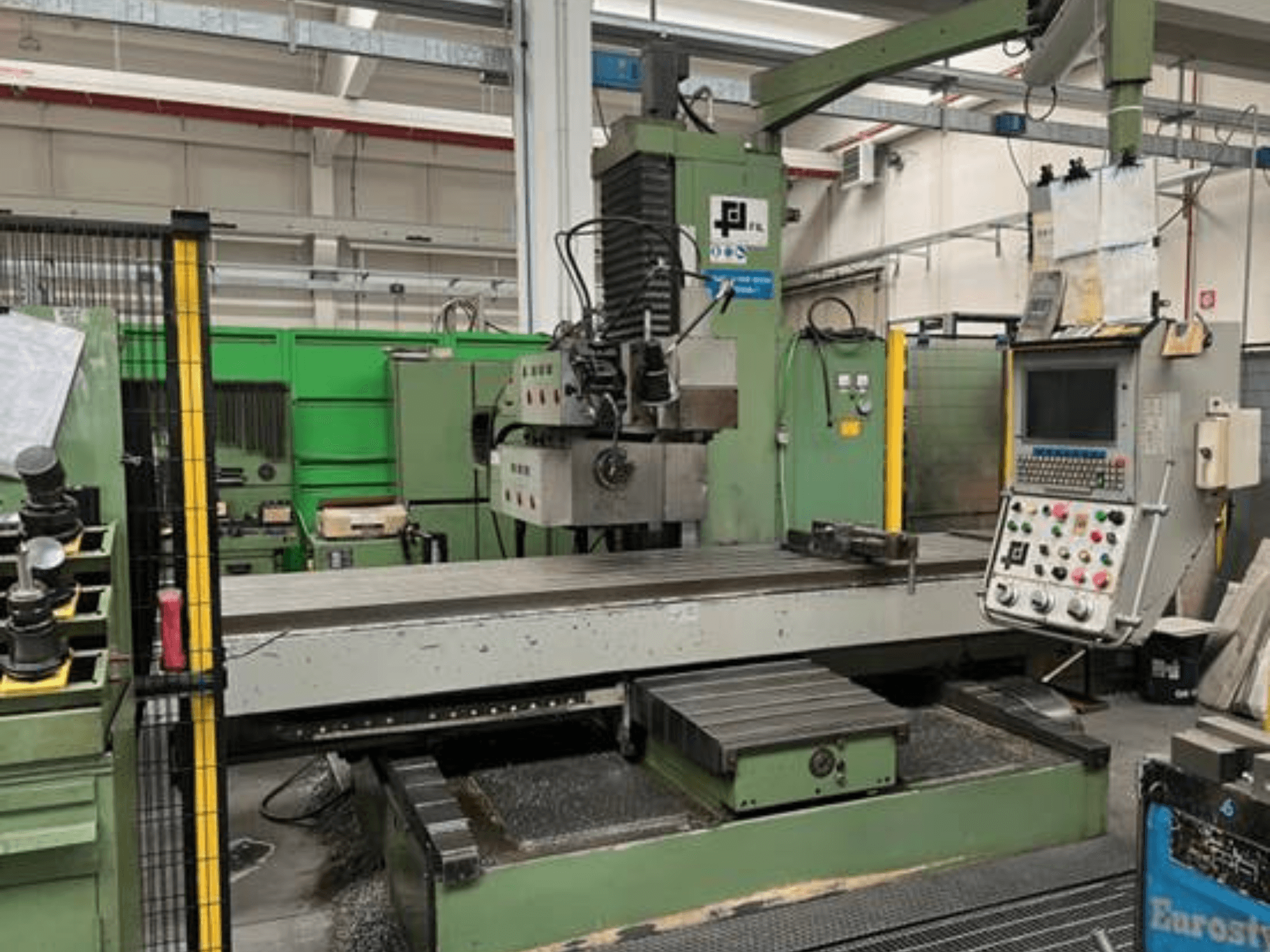 Industrijska glodalica tvrtke JFL, prednji pogled s upravljačkom pločom, velikim ravnim stolom i metalnim strugotinama na podu.