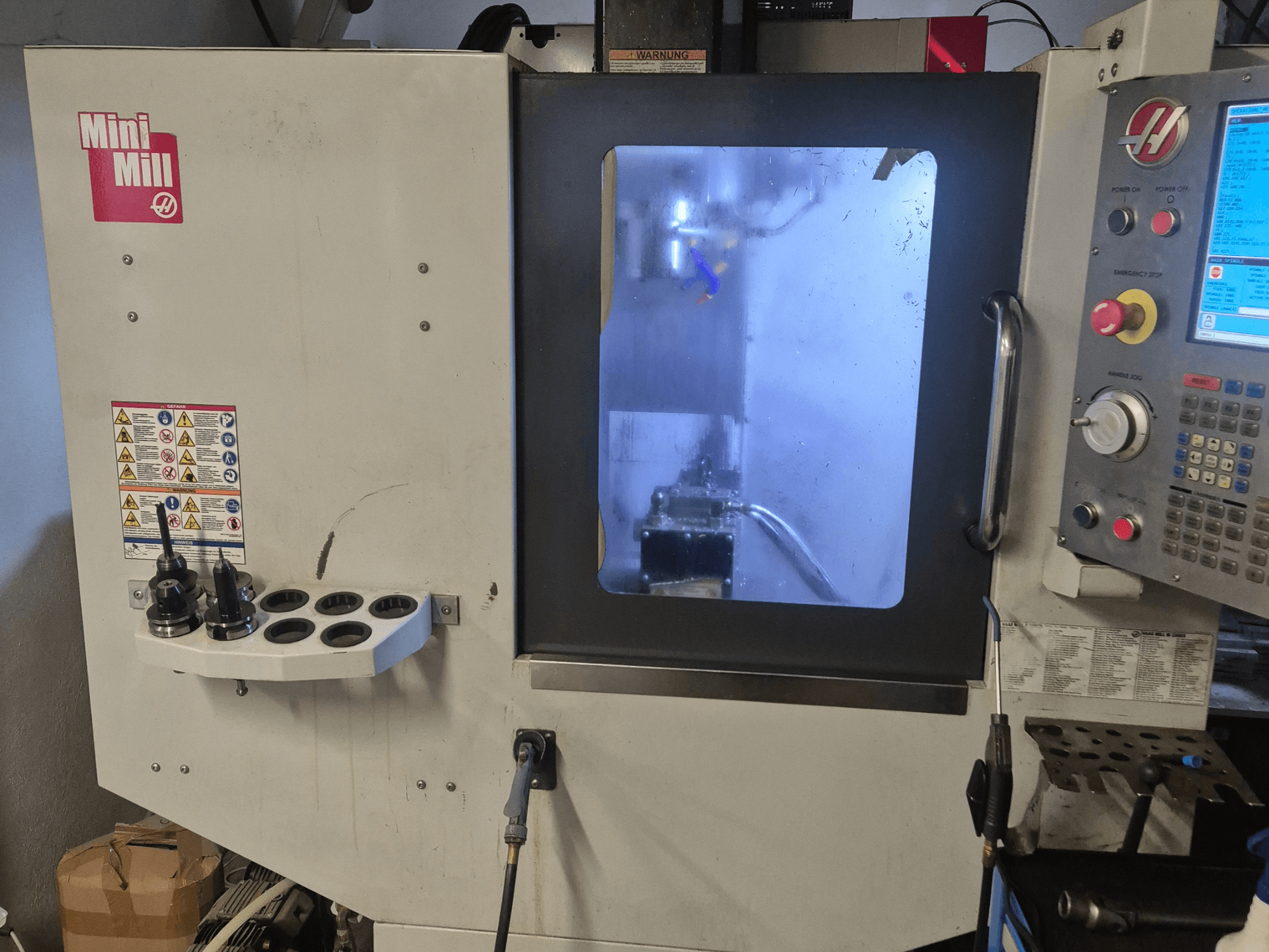 Prednji pogled na HAAS Mini Mill, s prikazom upravljačke ploče, držača alata i pogleda na područje obrade s rashladnom tekućinom.