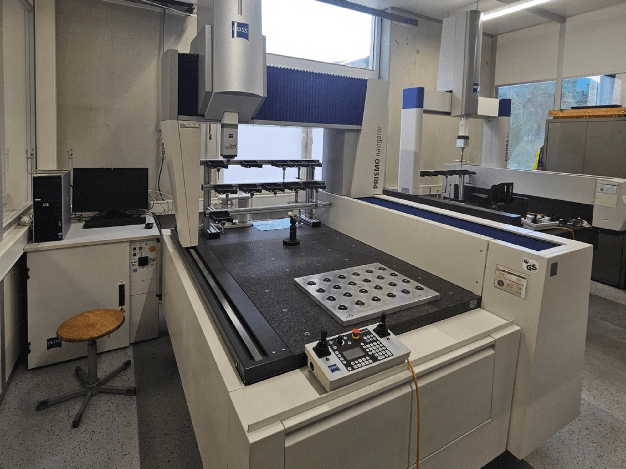 ZEISS Prismo Navigator 7 CMM u laboratoriju, prednji pogled koji prikazuje upravljačku ploču, radni stol i monitor.