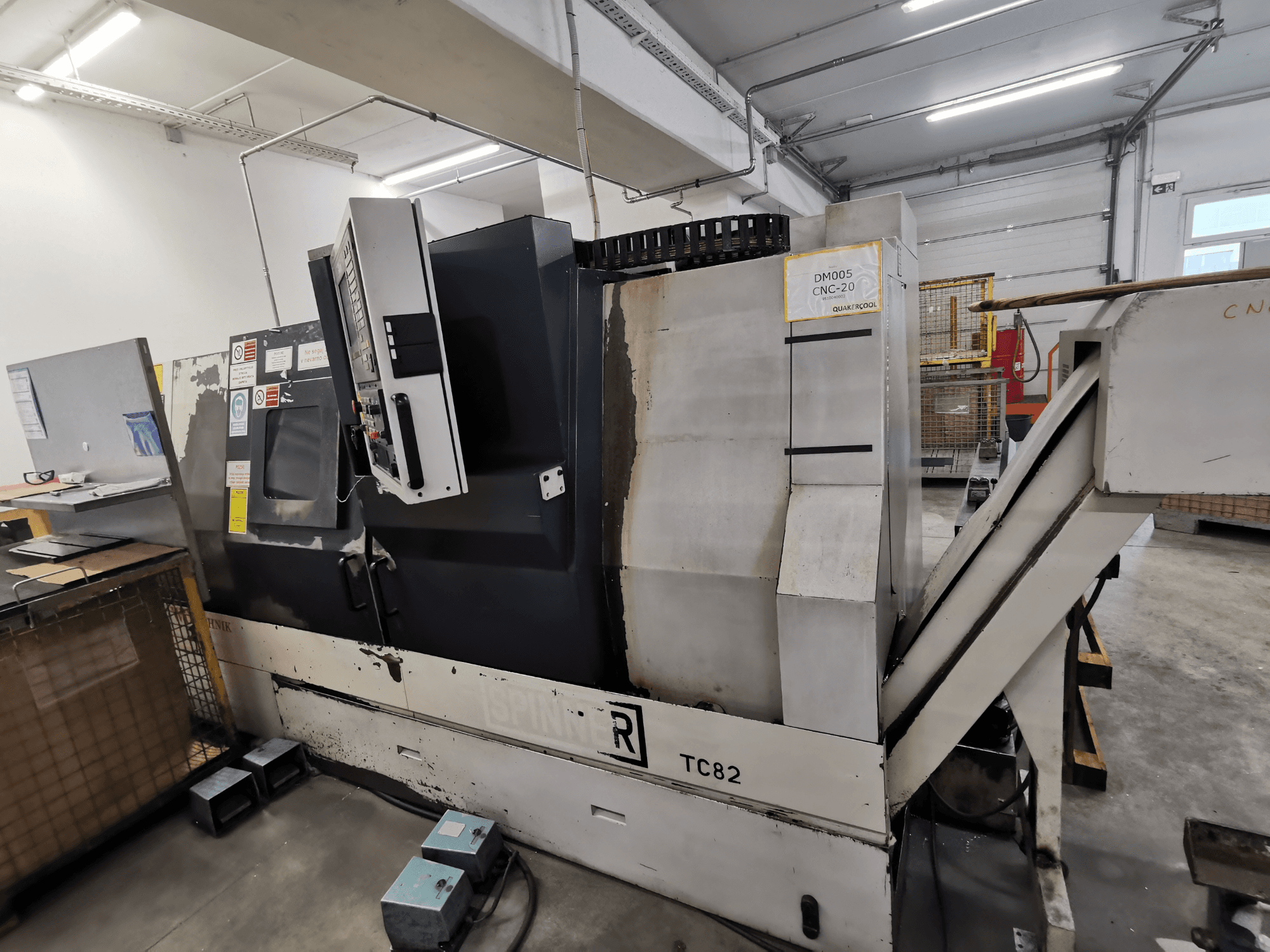 CNC stroj, marke Spinner, model TC82, bočni pogled koji prikazuje upravljačku ploču i žlijeb za uklanjanje otpada u radioničkom okruženju.