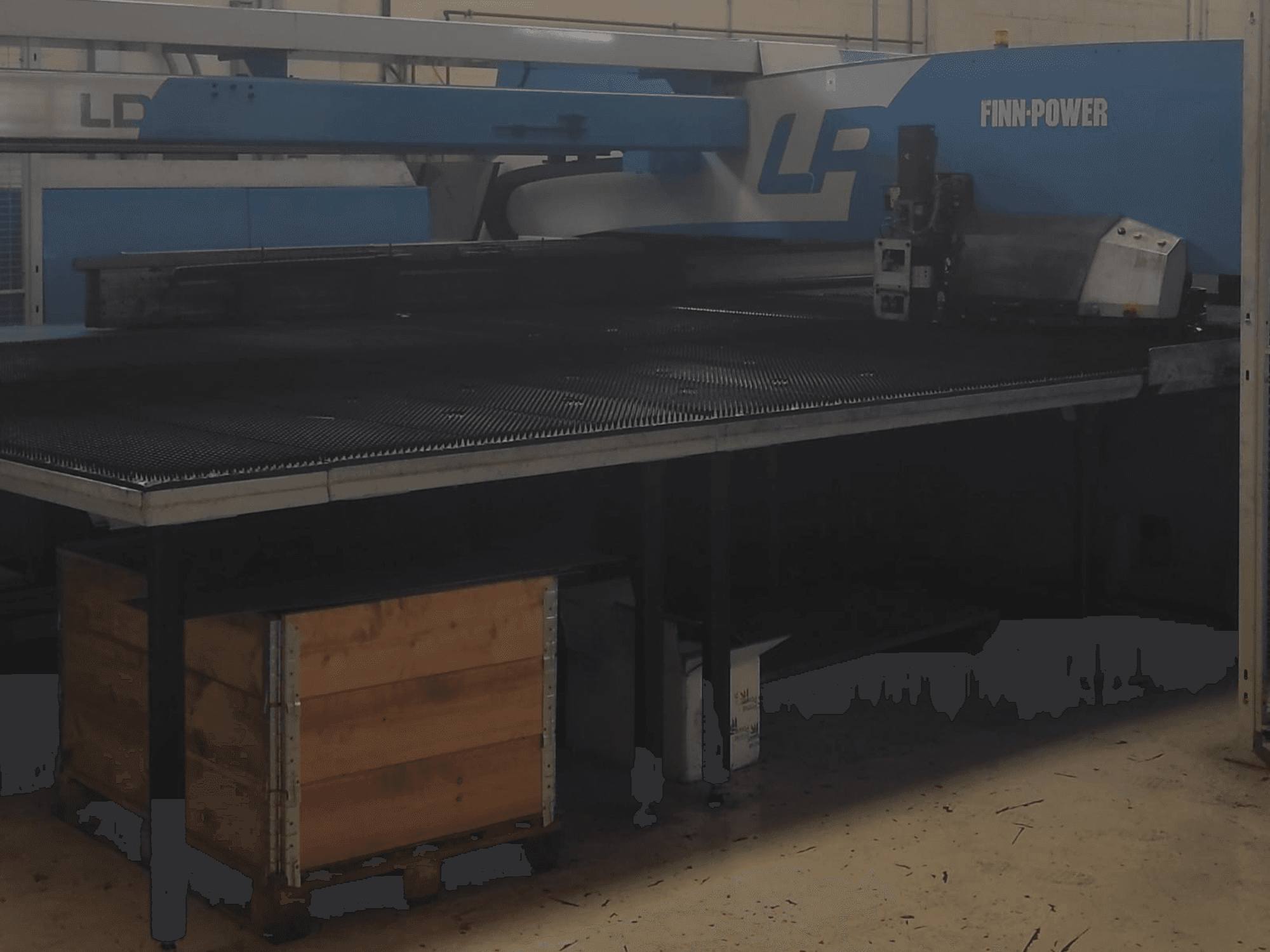 Finn-Power LP stroj za rezanje u tvornici, prednji pogled s teksturiranim metalnim stolom i drvenom kutijom ispod.