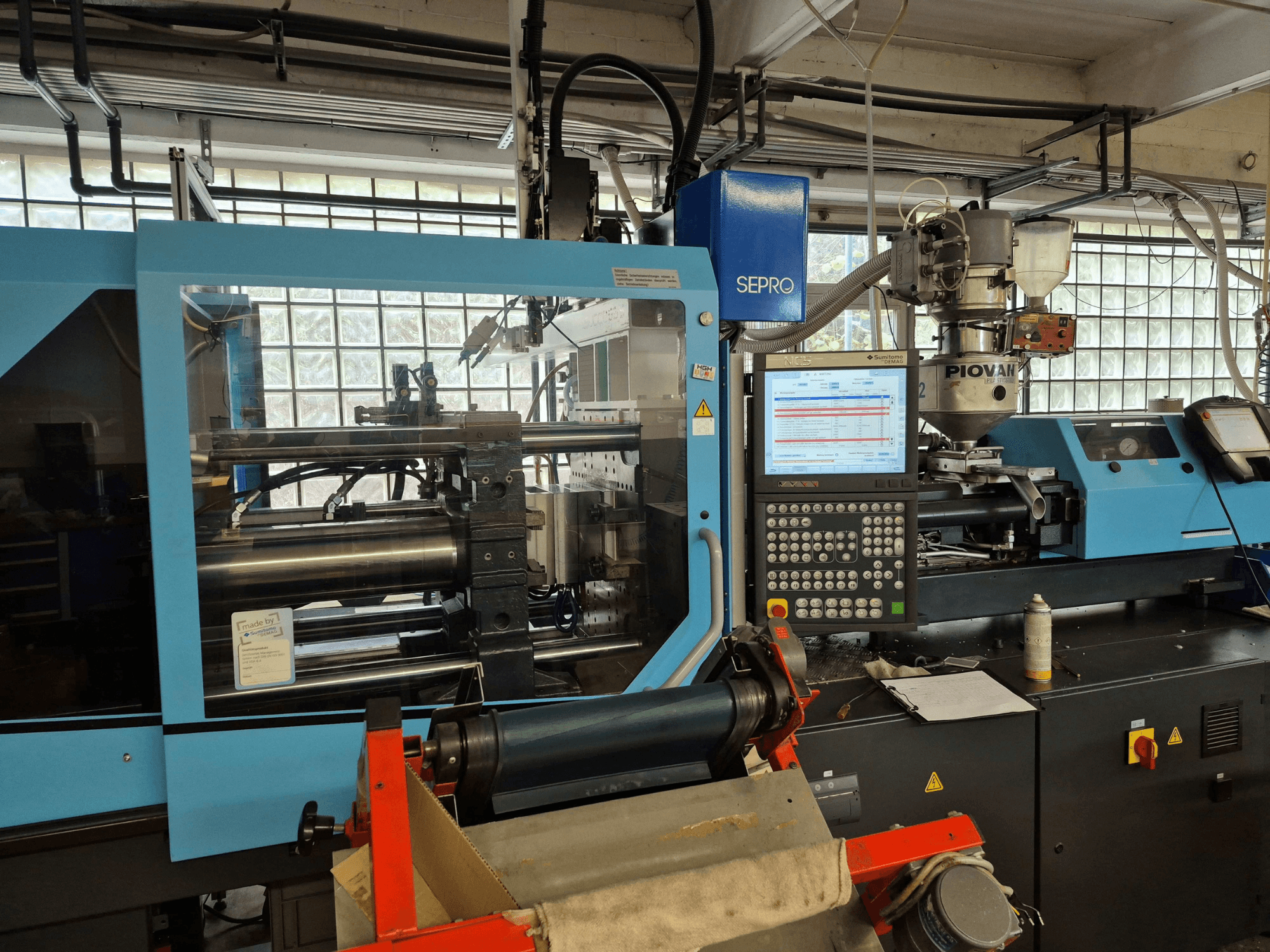 Hidraulički stroj za brizganje plastike SUMITOMO SHI DEMAG Systec 120/470-430, prednji pogled s vidljivom upravljačkom pločom i sustavom za dovod.