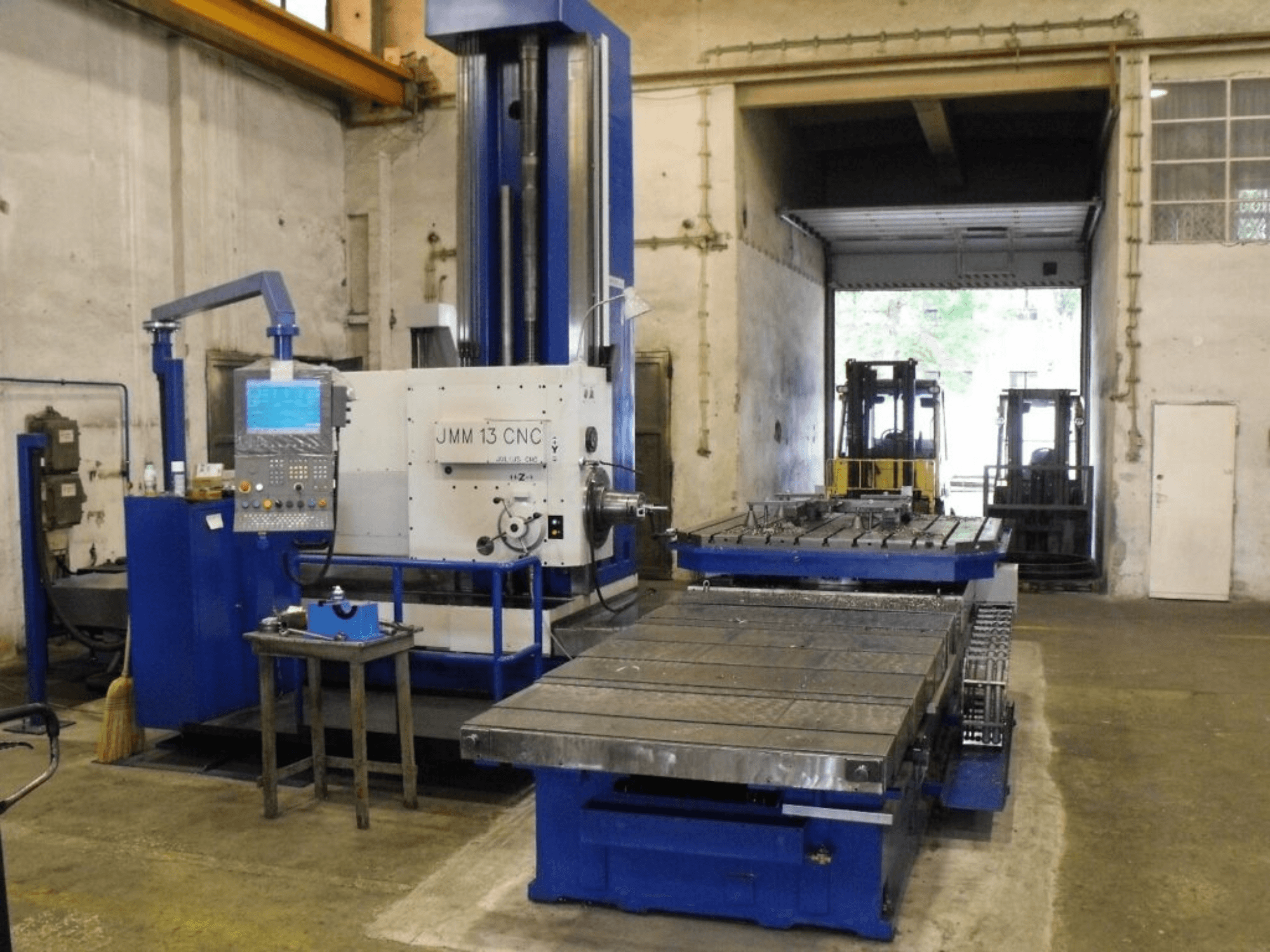 CNC glodalica JMM 13 u radionici, prednji pogled, ima upravljačku ploču, veliki radni stol i industrijsku pozadinu.