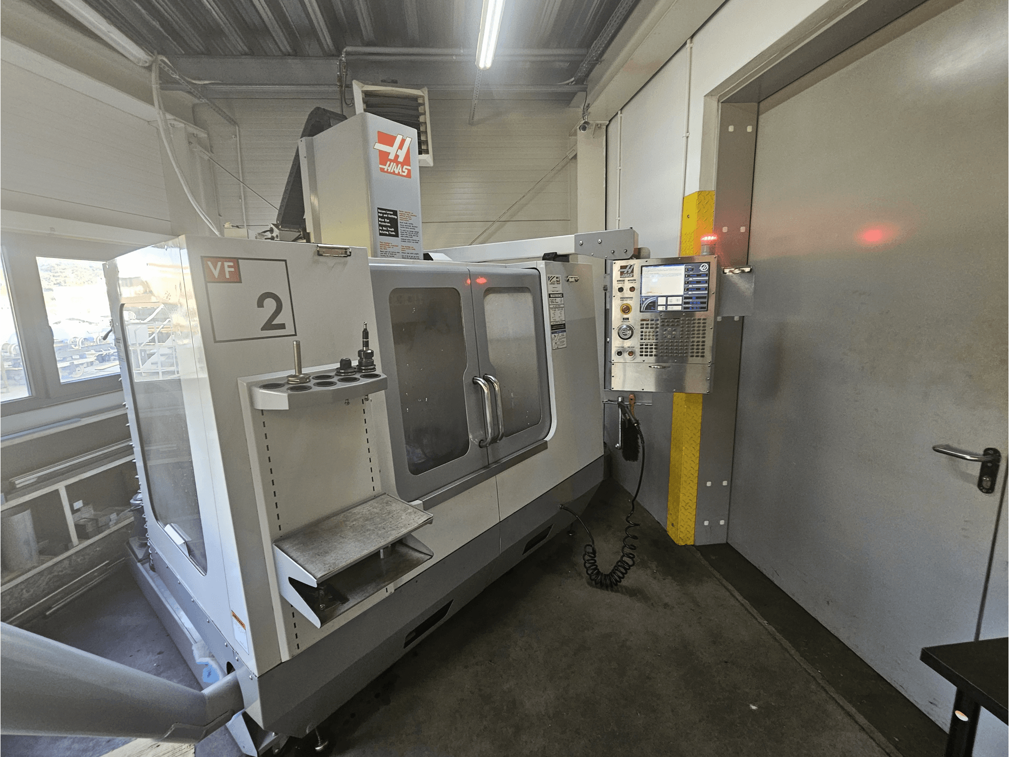 Haas VF-2 CNC glodalica, prednji pogled, prikazuje upravljačku ploču, držače alata i prozirni prozor na radnom prostoru.