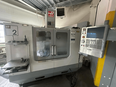 Haas VF-2 CNC stroj, prednji pogled, s upravljačkim elementima, držačem alata i prozirnim vratima s vidljivim alatima unutar ormara.