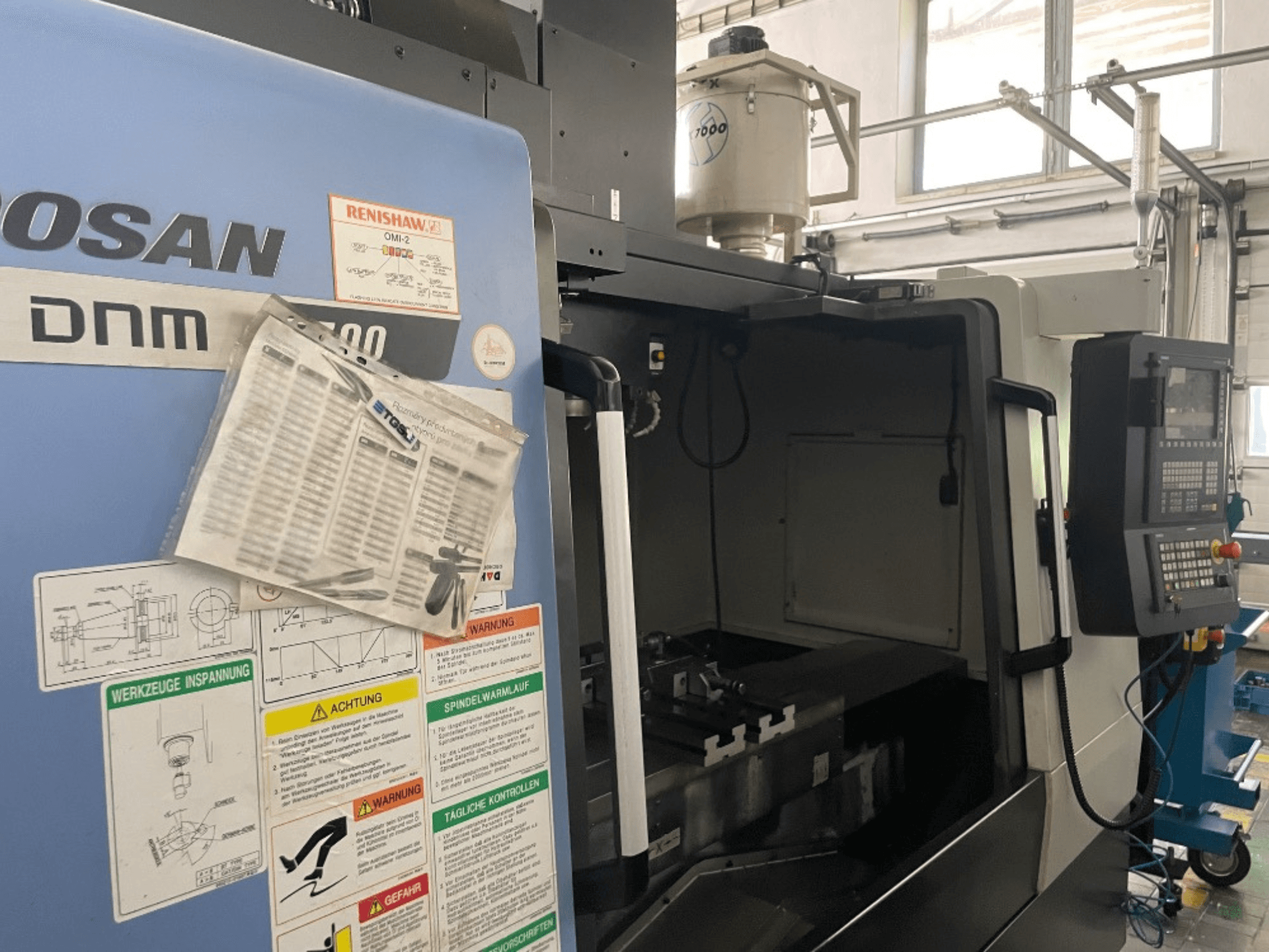 Vertikalni obradni centar DOOSAN DNM 5700, prednji pogled, prikazuje upravljačku ploču, sigurnosne naljepnice i detalje stroja.