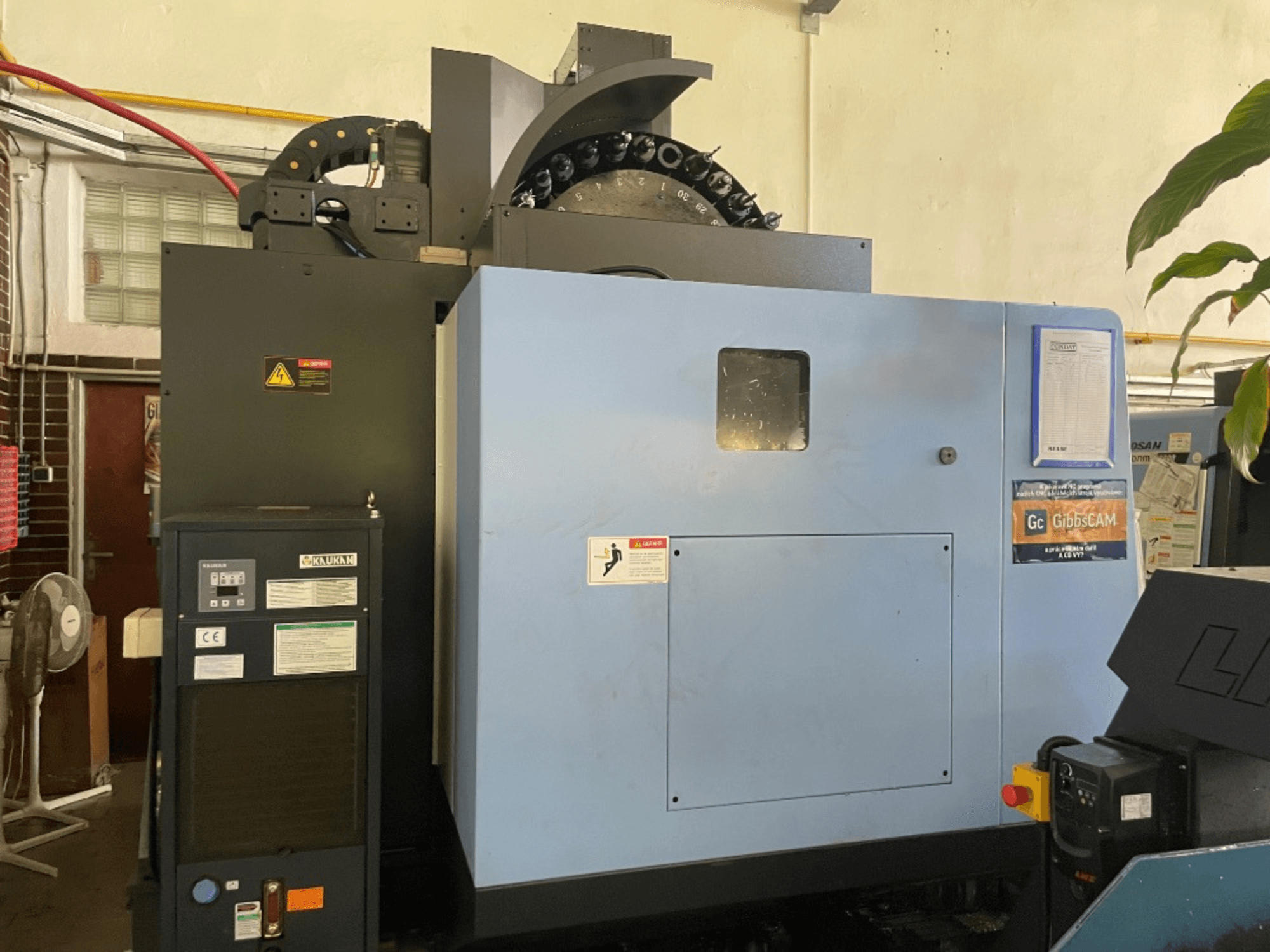 Prednji pogled na vertikalni obradni centar DOOSAN DNM 5700, s prikazom upravljačke ploče, sigurnosnih naljepnica i značajki stroja.