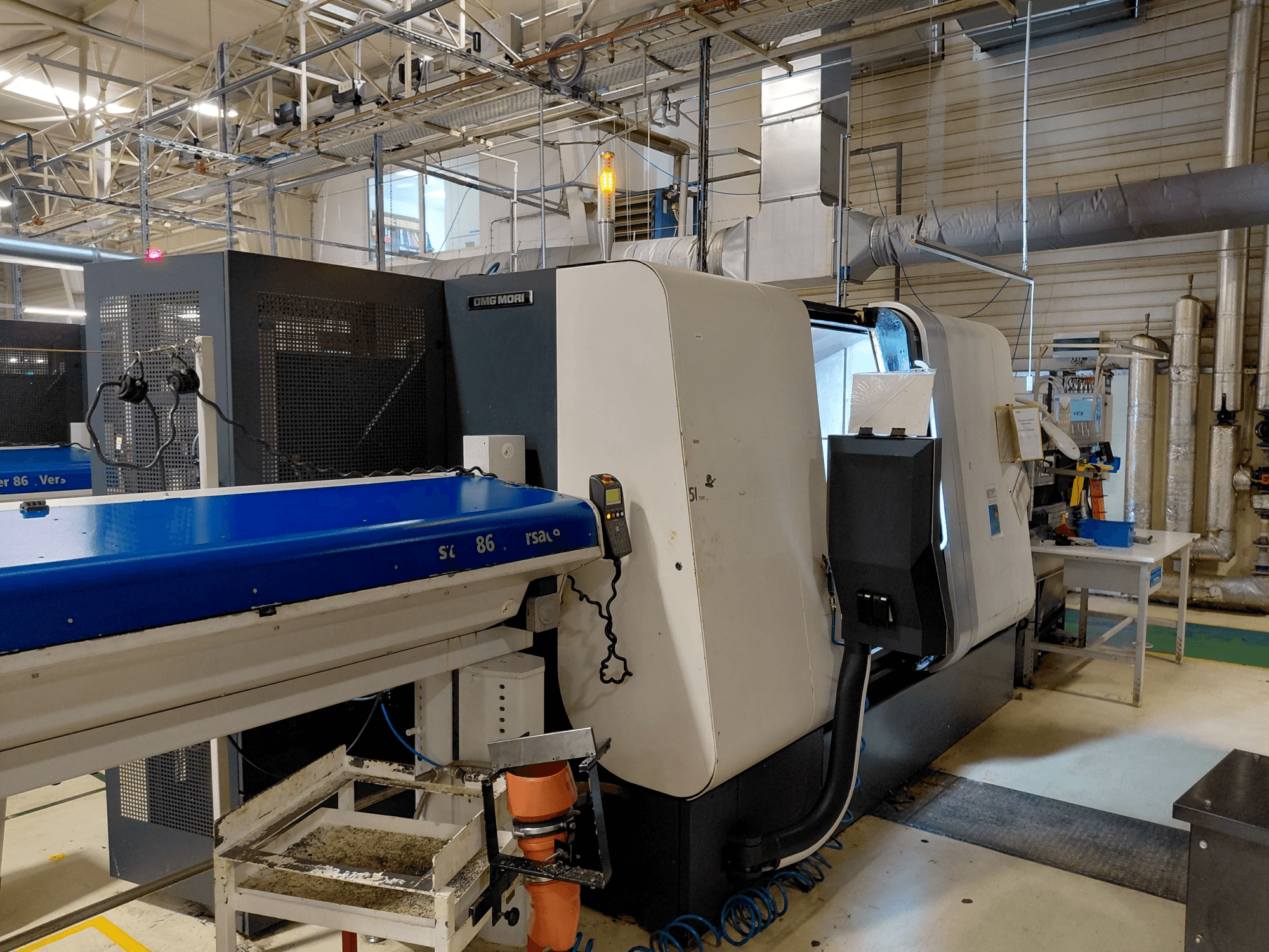 DMG MORI Sprint 65 linearni viševretenski tokarski stroj, bočni pogled s upravljačkom pločom i transporterom vidljivim u radioničkom okruženju.