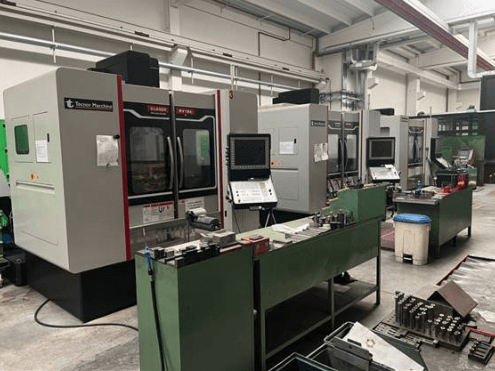 Četiri CNC stroja tvrtke Tecnoer Marchine u radionici, prednji pogled, s alatima i dijelovima na zelenim radnim stolovima.