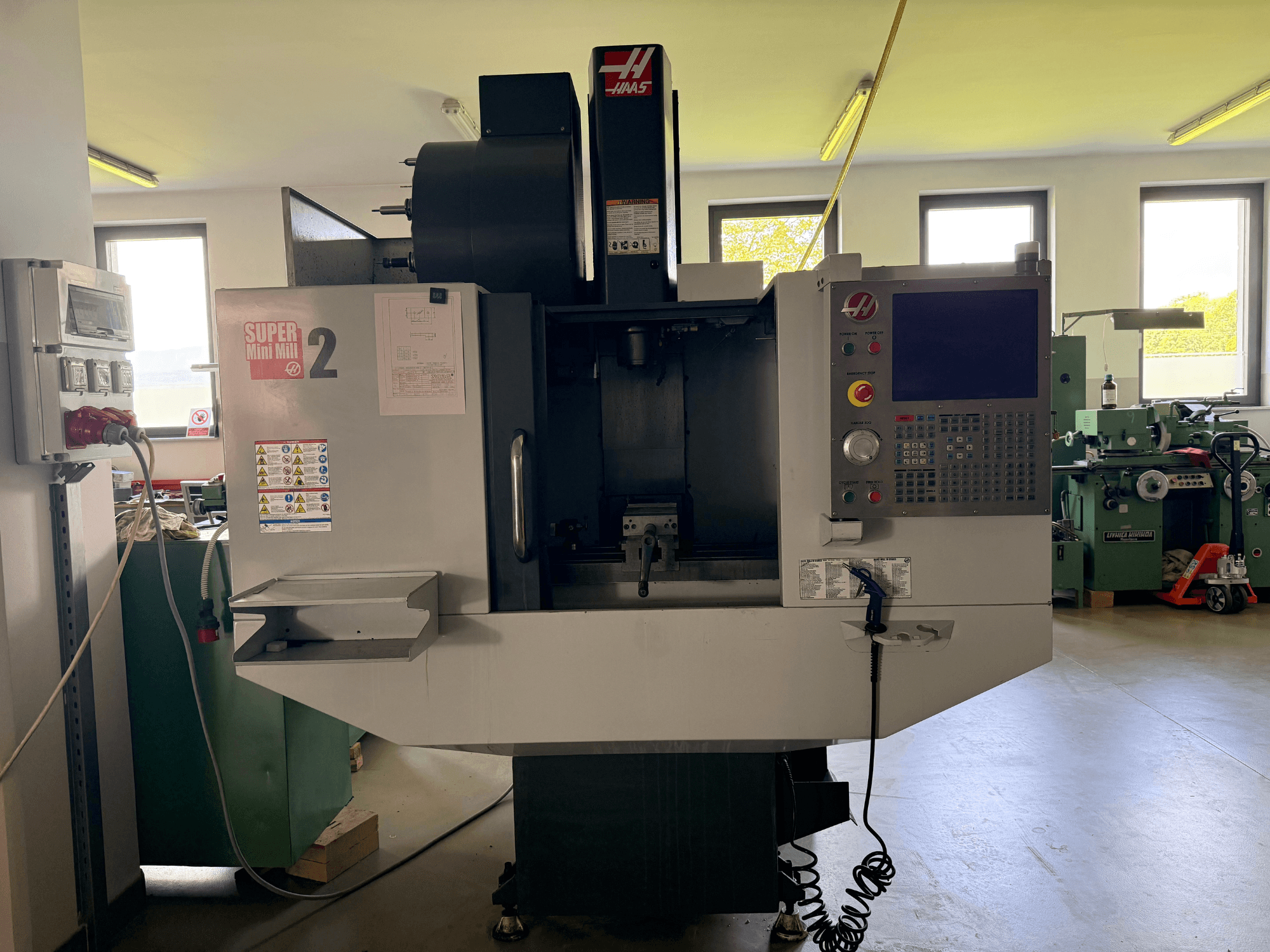 Vertikalni obradni centar Haas Mini Mill 2 u prednjem pogledu, s prikazom upravljačke ploče i područja alata s naljepnicama upozorenja.